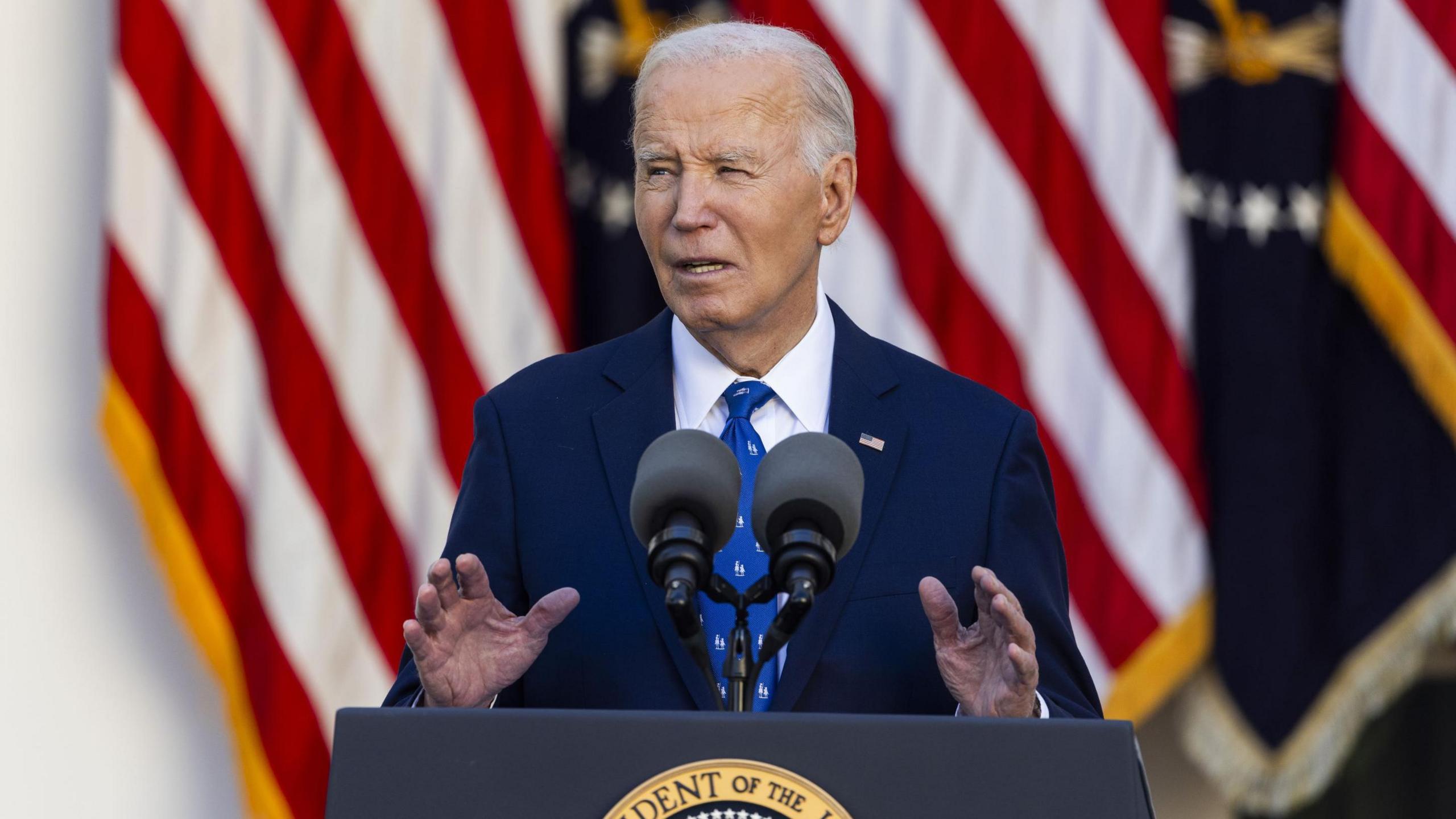 US President Joe Biden speaks at a lectern in front of US flags