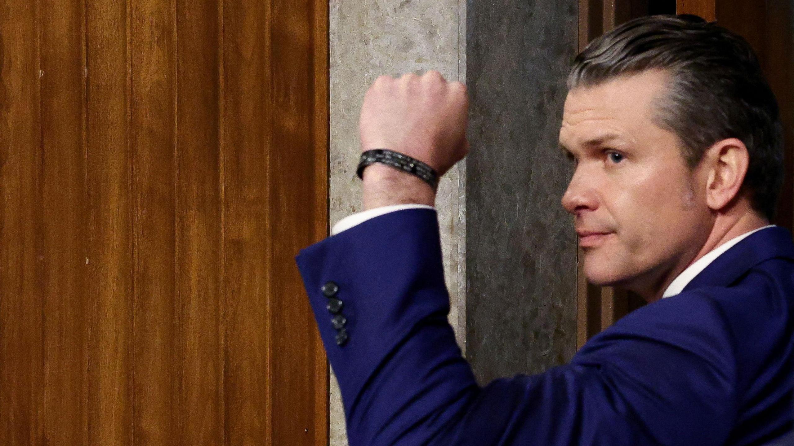 Pete Hegseth holds his fist in the air as he glances to his left.