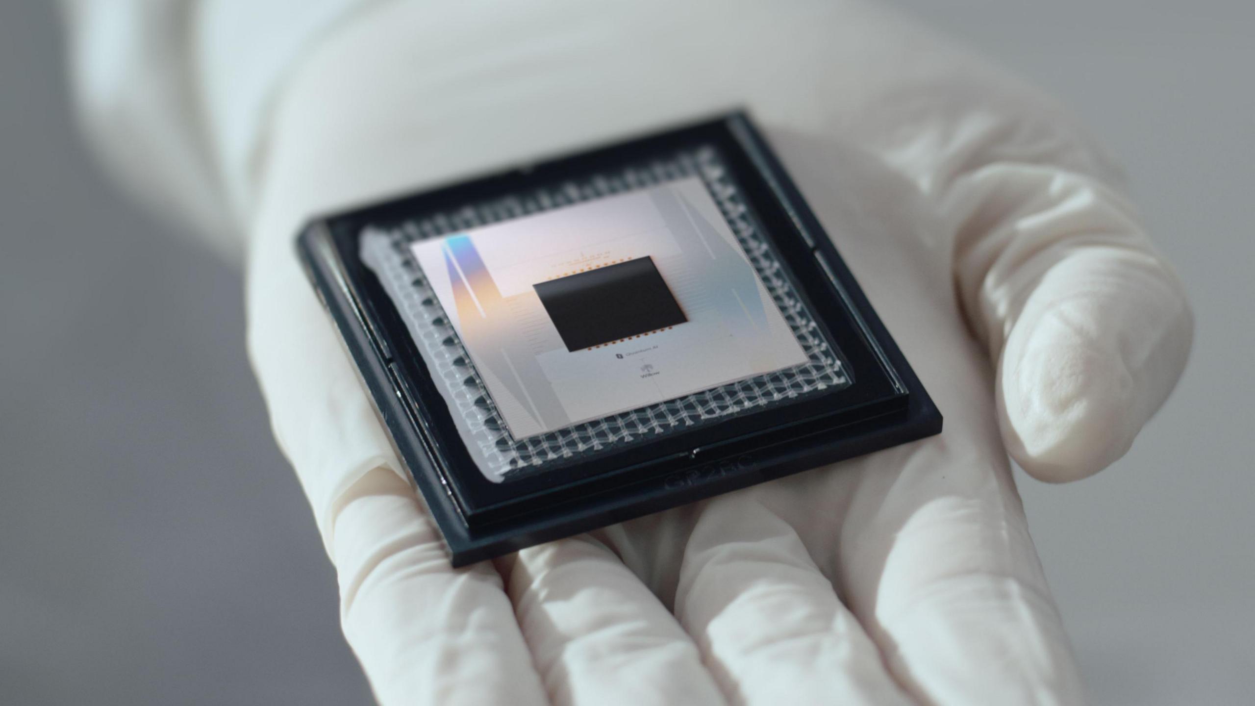 A picture of Google's Willow chip sitting in the palm of a white gloved hand. The chip - about the size of a pub coaster - resembles nested black, silver, then black squares.