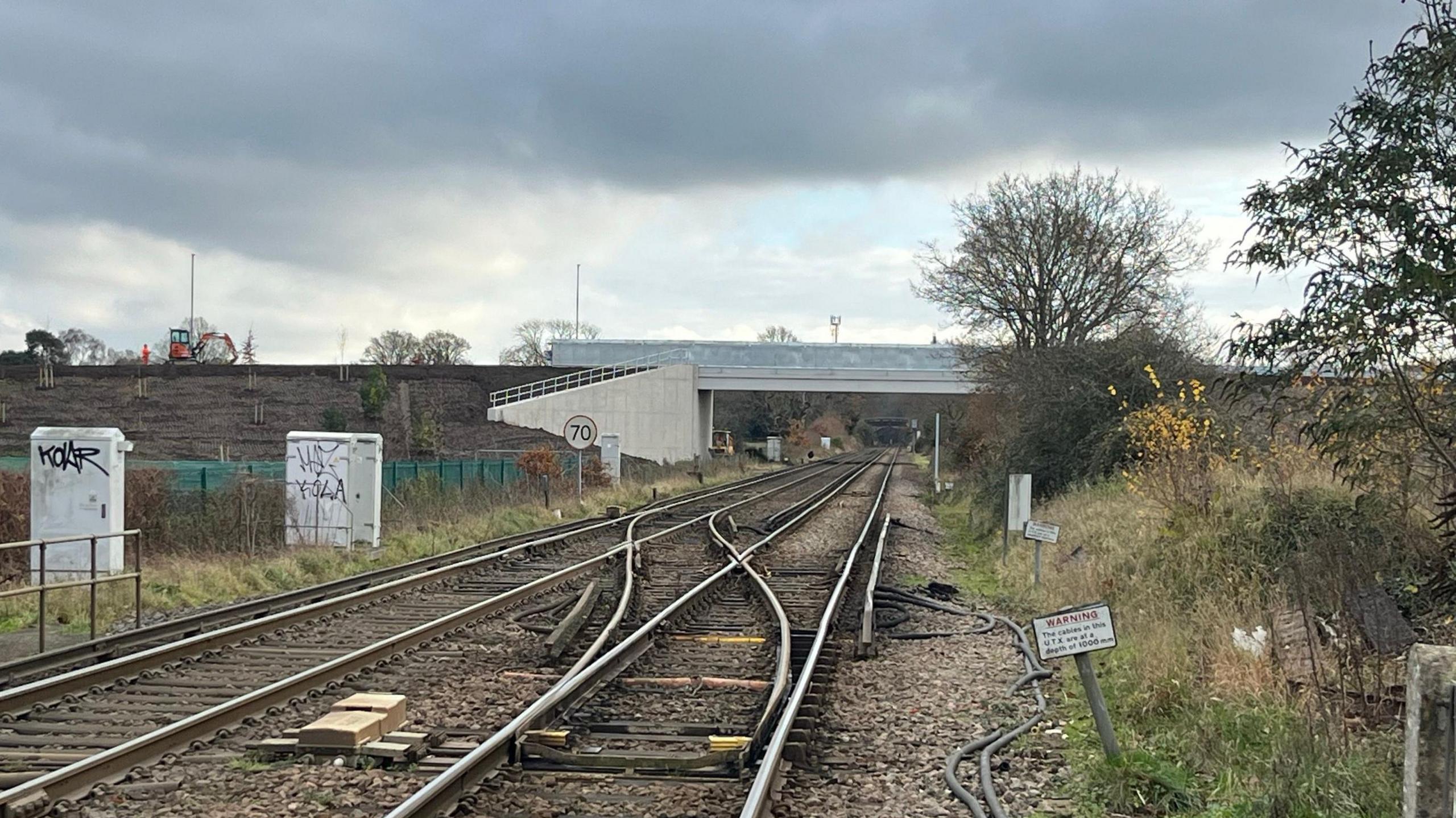 Rail tracks at Ash, with the new bridge in the distance. Also trees and undergrowth are visible.