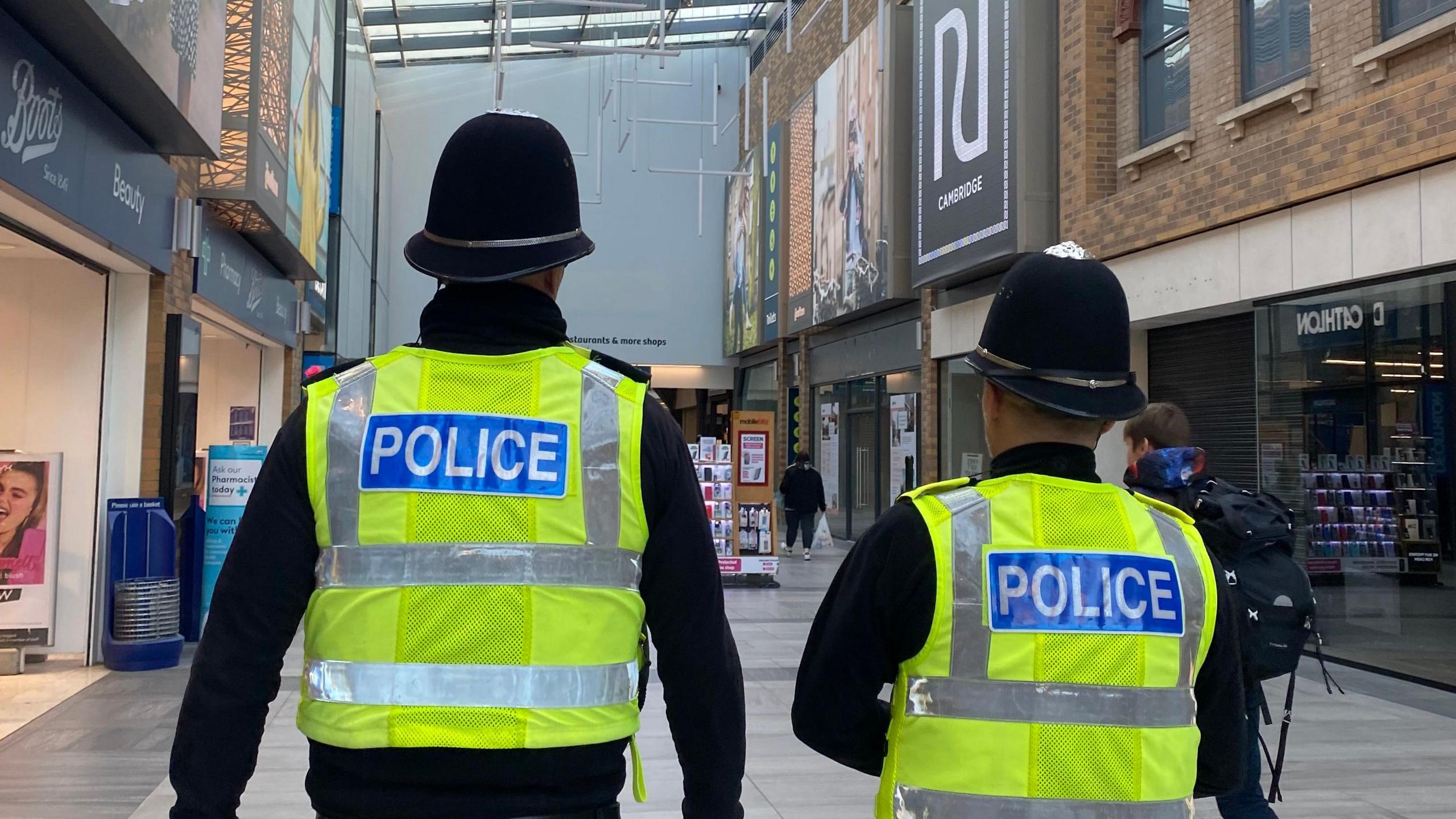 Two police officers with their back to camera- wearing their high-vis green and black uniforms 