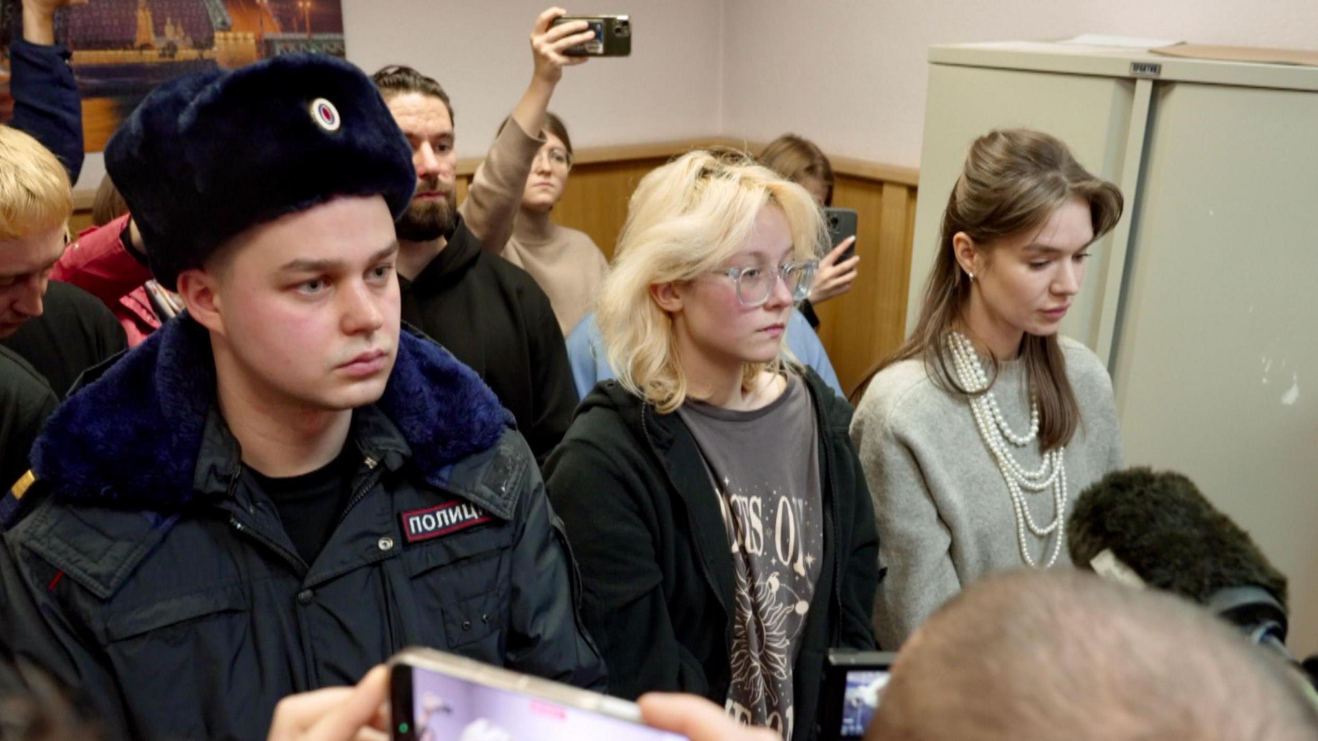 Diana Loginova, centre, stands in coutr flanked by a police officer and her lawyer