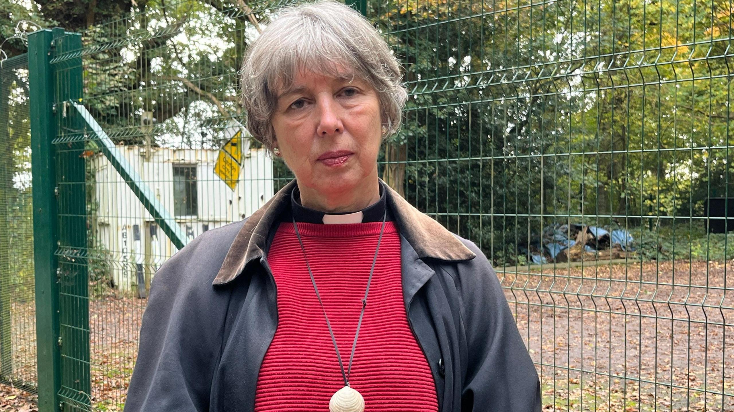 A priest in a dog collar with a red jumper looking unhappy