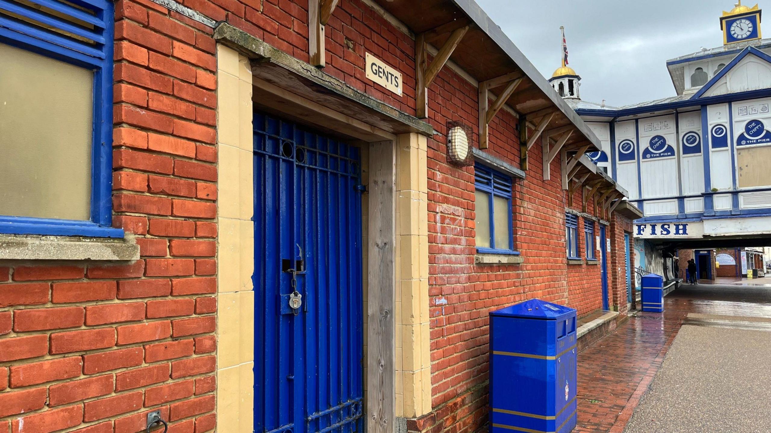 A padlocked public toilet on Eastbourne seafront, in front of a fish and chip shop.