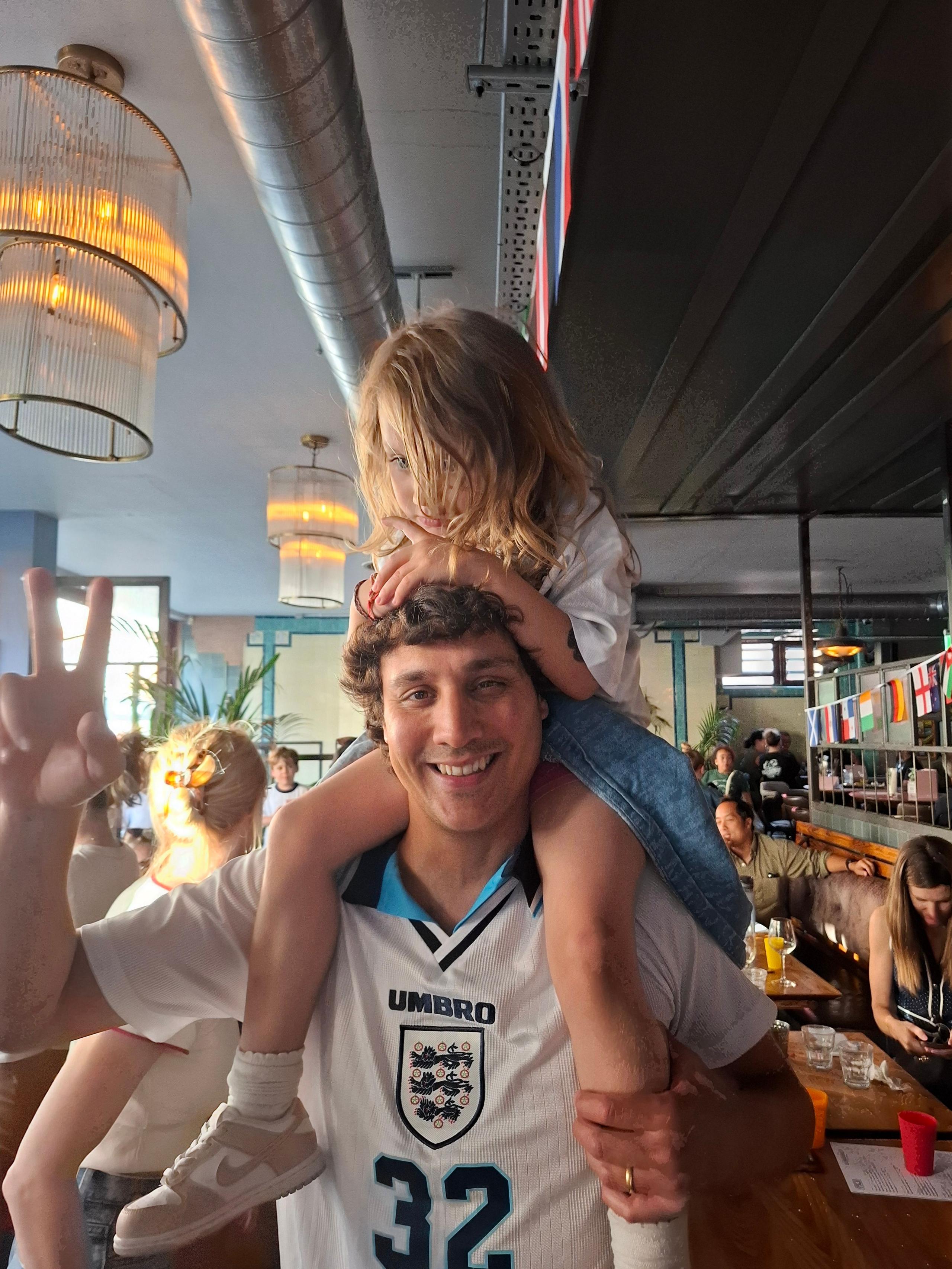 Tomal Syed-Aguirre holds his daughter Marla on his shoulders, while wearing a Euro 96 shirt with 32 on the front, in a pub in West Norwood, London.