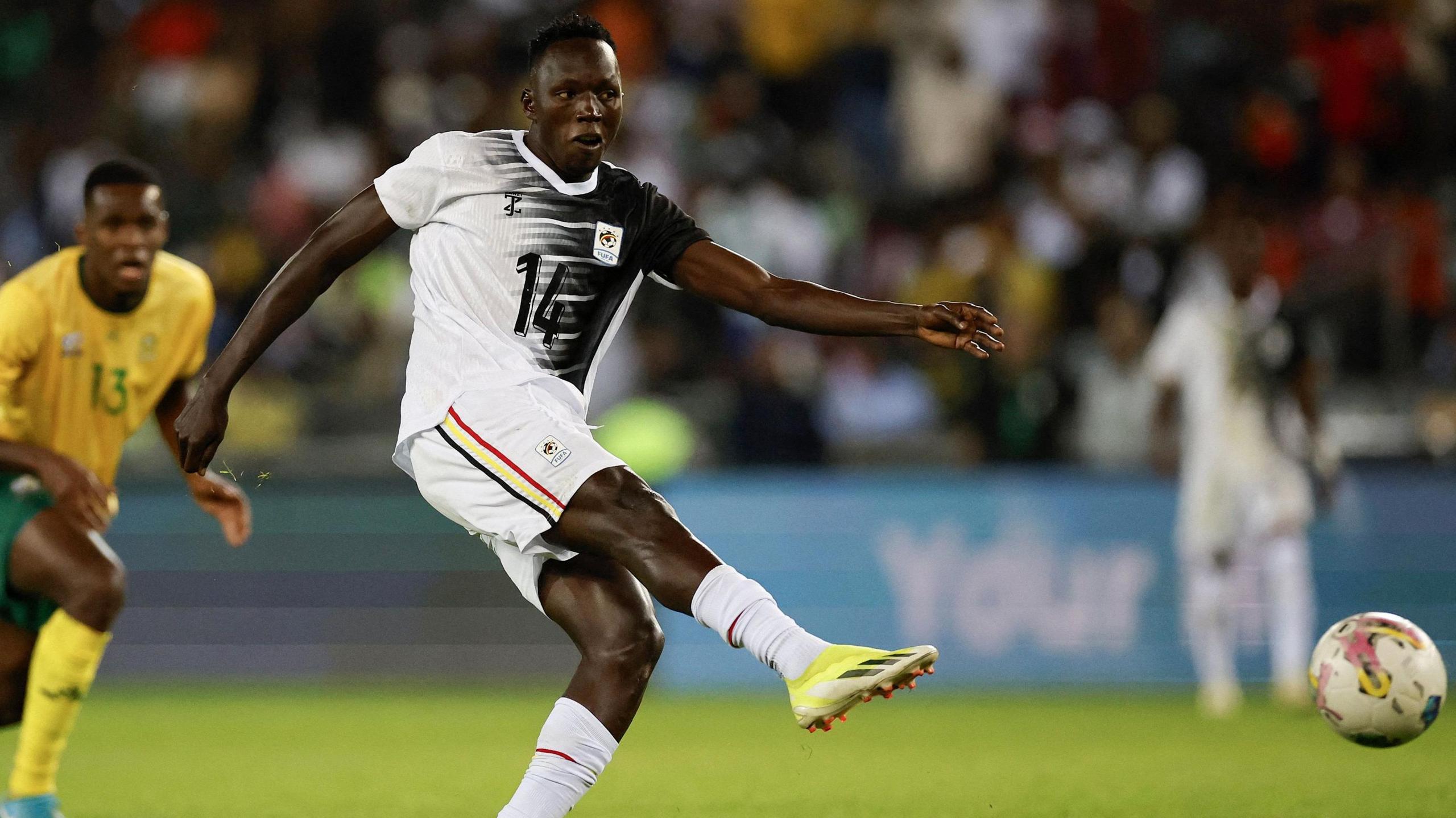 Uganda forward Denis Omedi fires a right-footed shot towards goal, with the ball in the bottom right of the picture