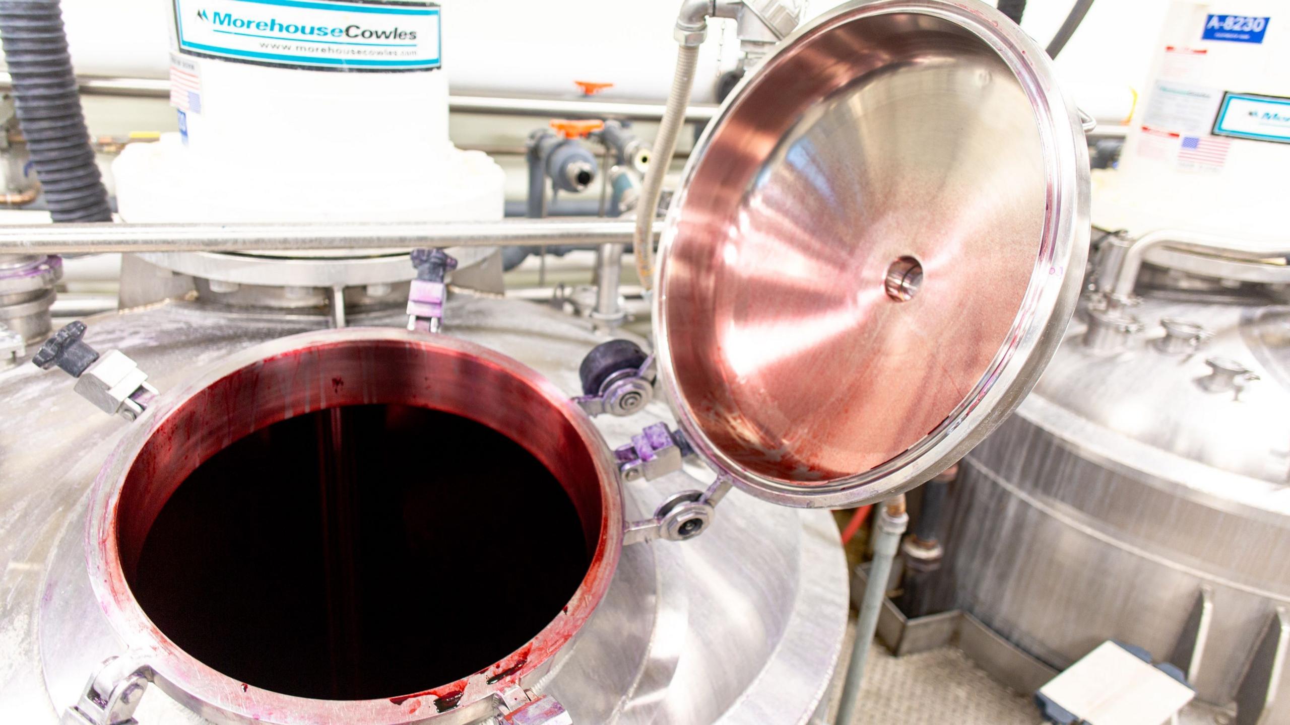 The open lid of a large stainless steel vat reveals a deep-red coloured liquid.