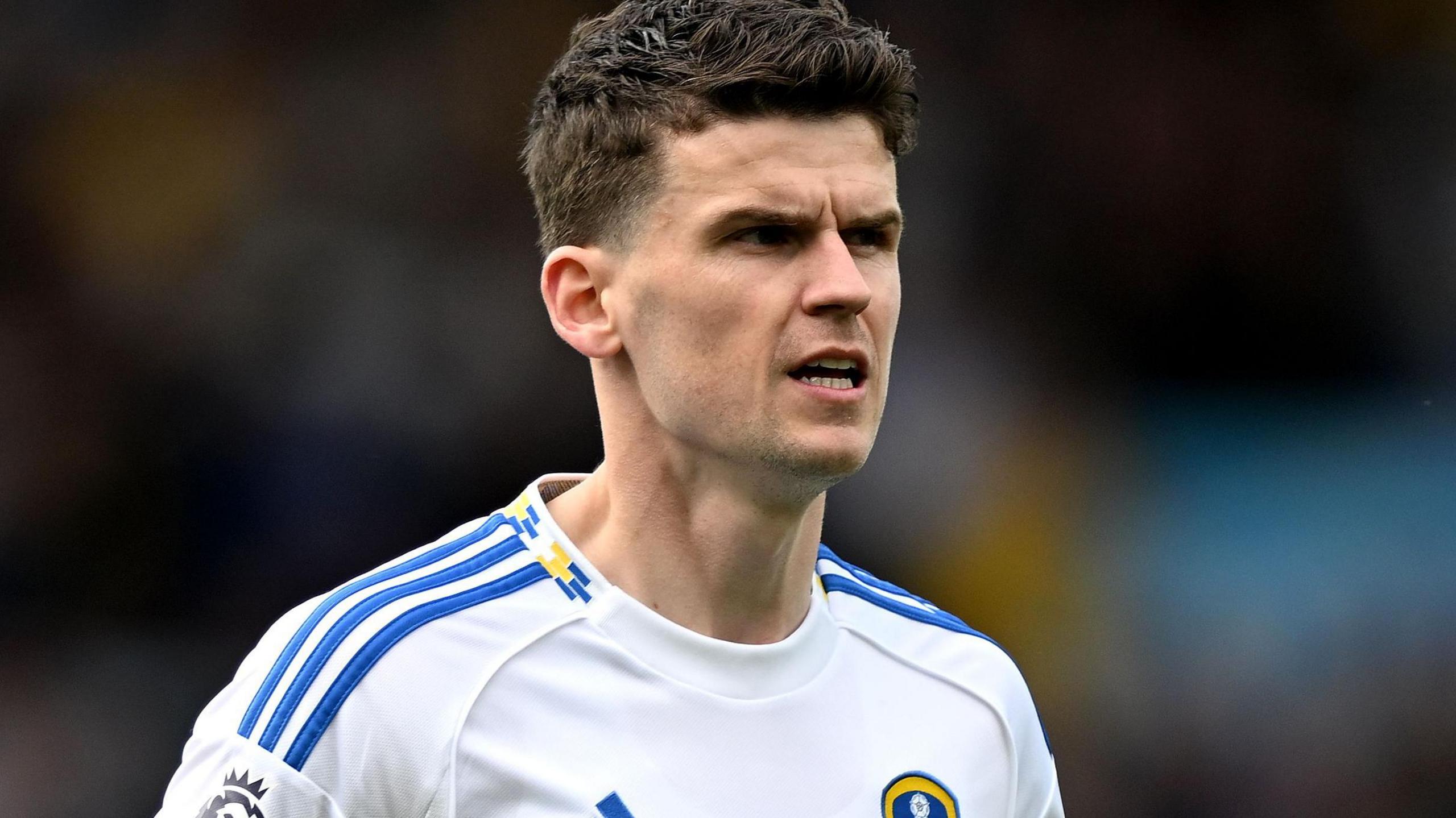 Sam Byram wearing a Leeds shirt looks to his right with a slightly open mouth