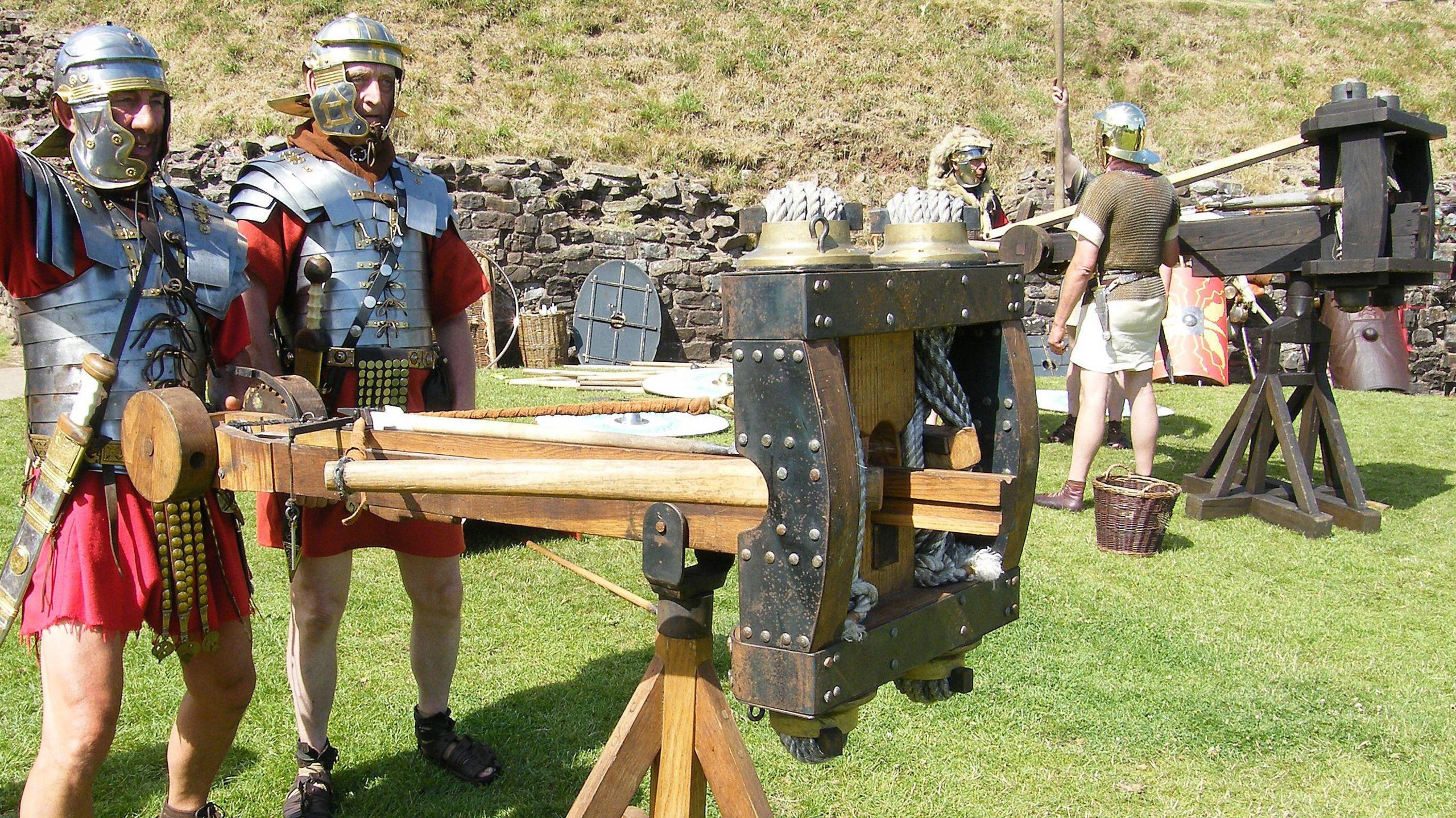 Roman military reenactors with two reconstructed Roman artillery pieces, both resembling large wooden crossbows on stands.