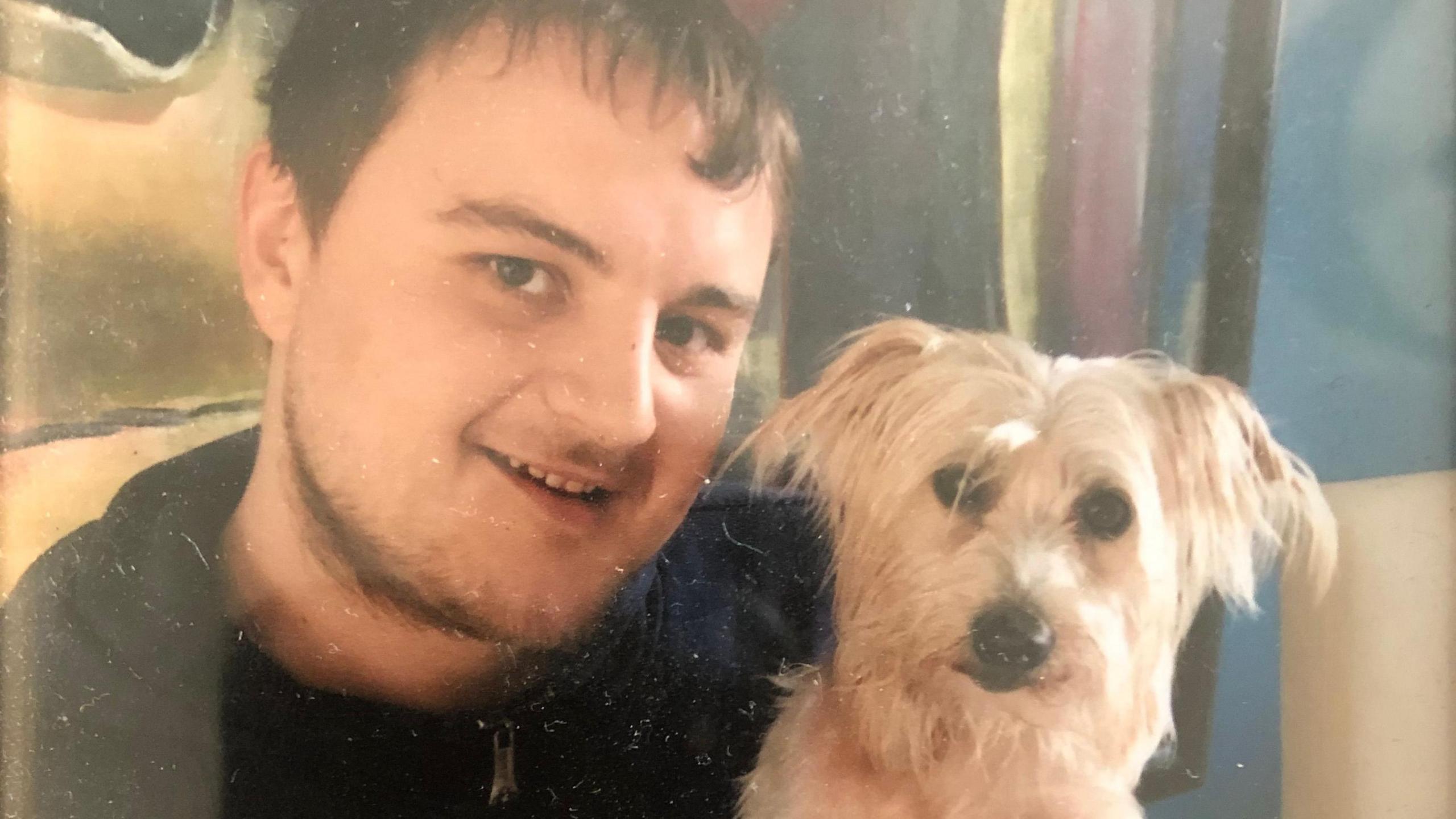 Arthur Hölscher Ermert, with short dark hair and a fringe, gives an open-mouthed smile to the camera. He's cuddling a small white dog.