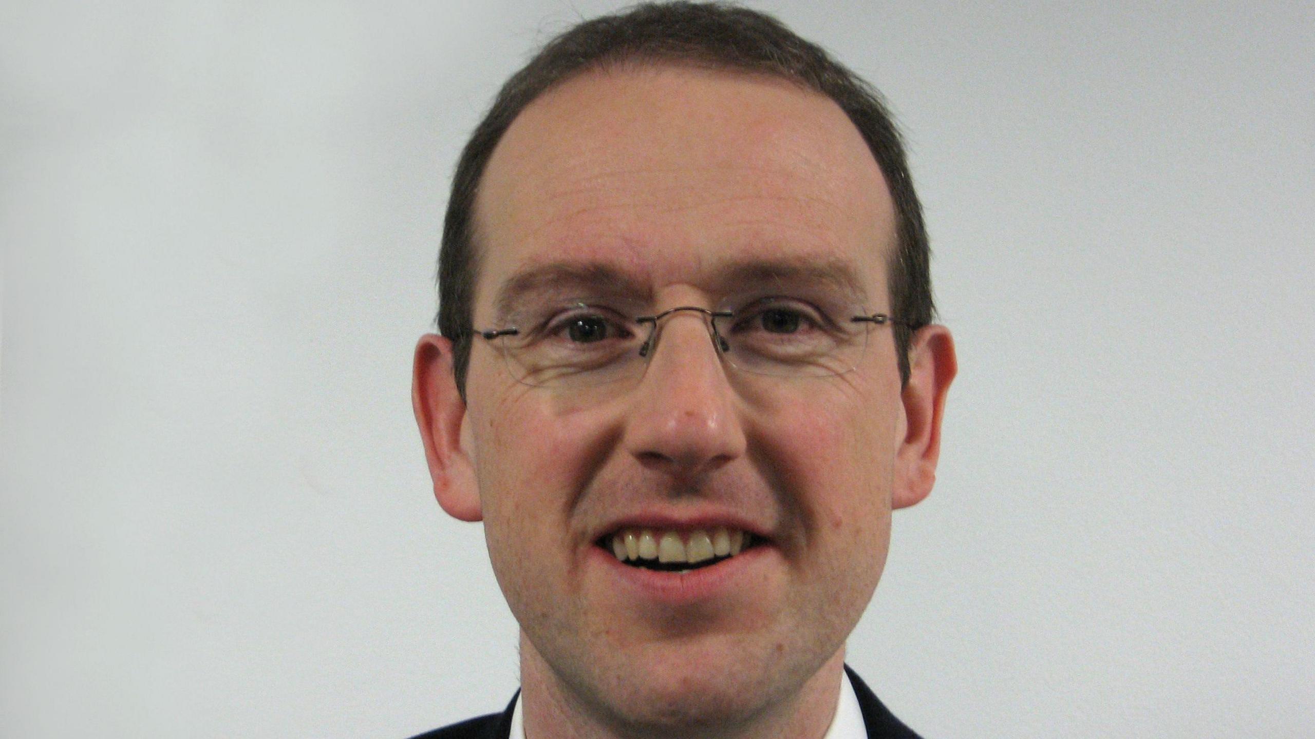 Plaid Cymru politician Llyr Gruffydd, who has thin glasses and brown hair. It is a shot of his head.