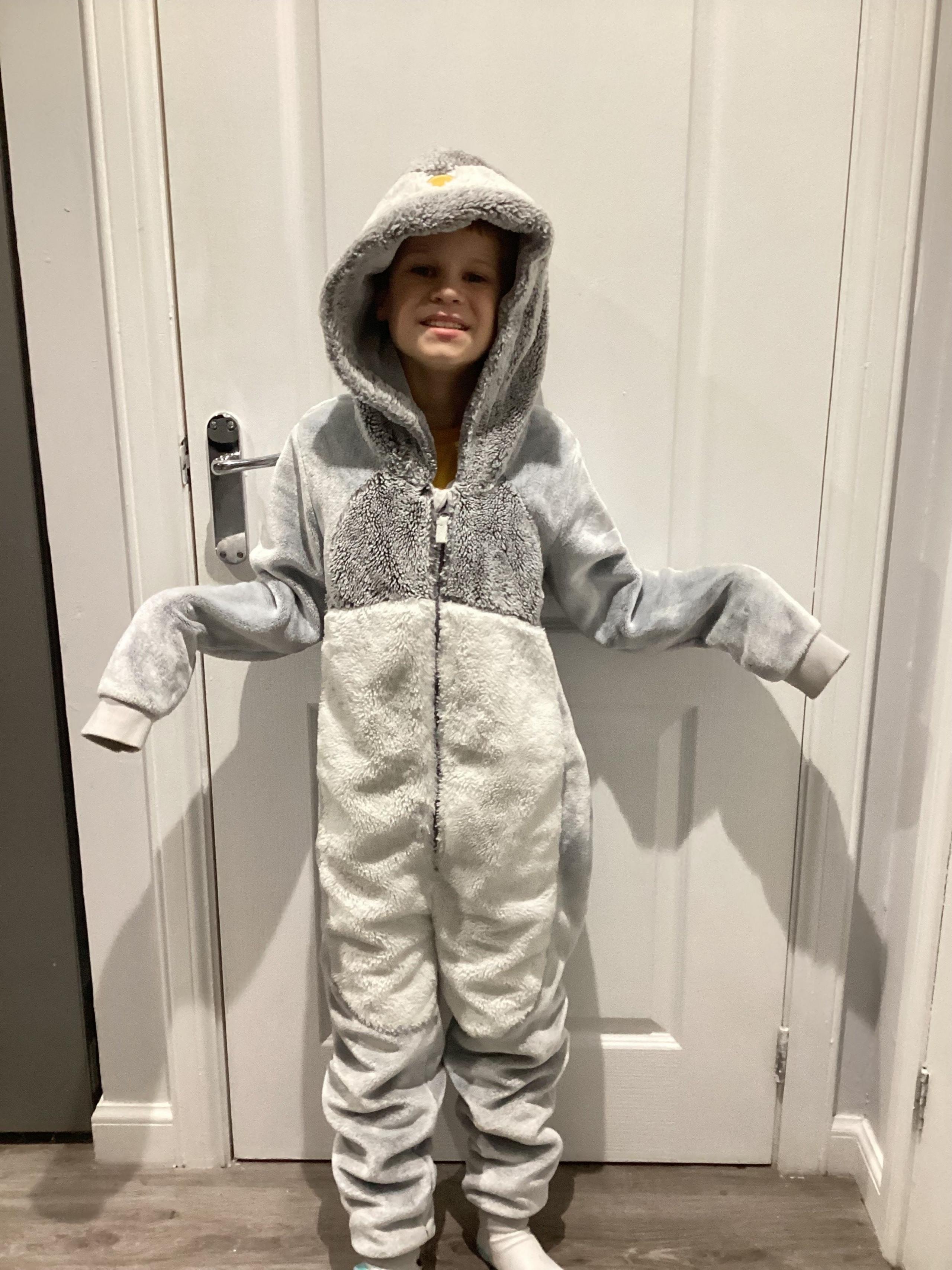 A boy stands in front of a door and wears a penguin onesie