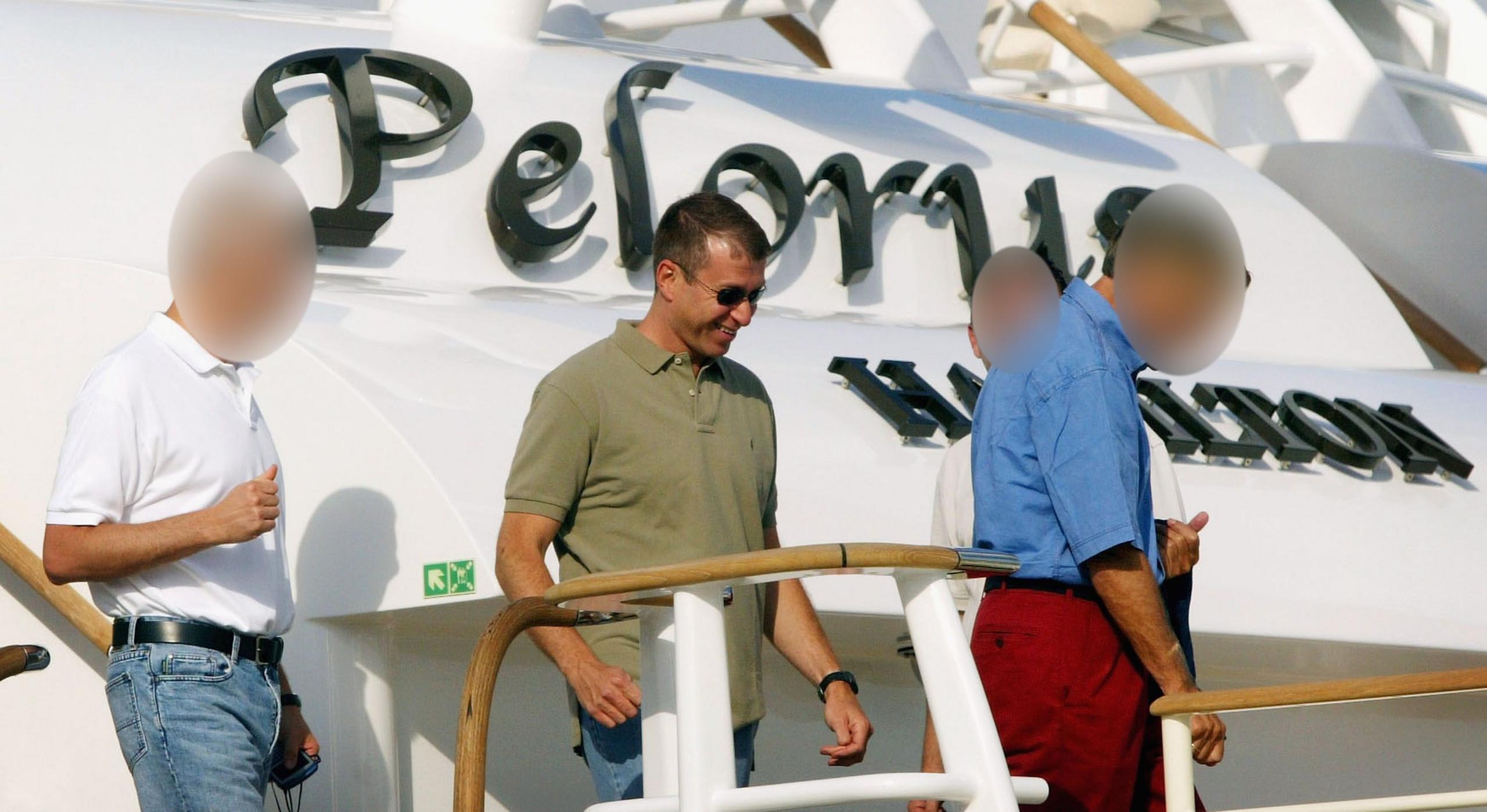 Roman Abramovich, wearing sunglasses, jeans and a khaki polo shirt, stepping off the deck of the Pelorus with some associates, with the yacht's name visible behind him