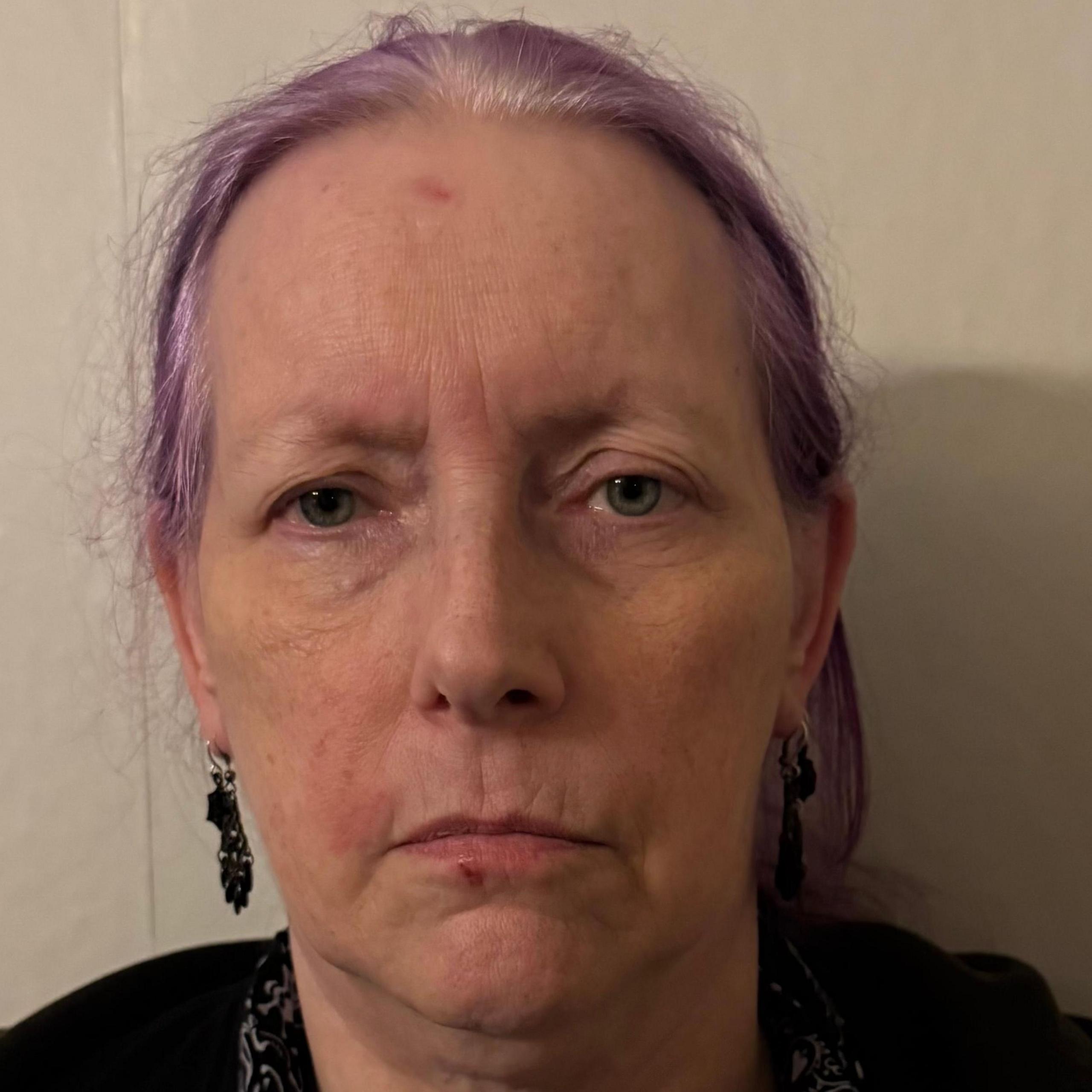 Carol Wood looking directly at the camera. She has purple hair and black earrings