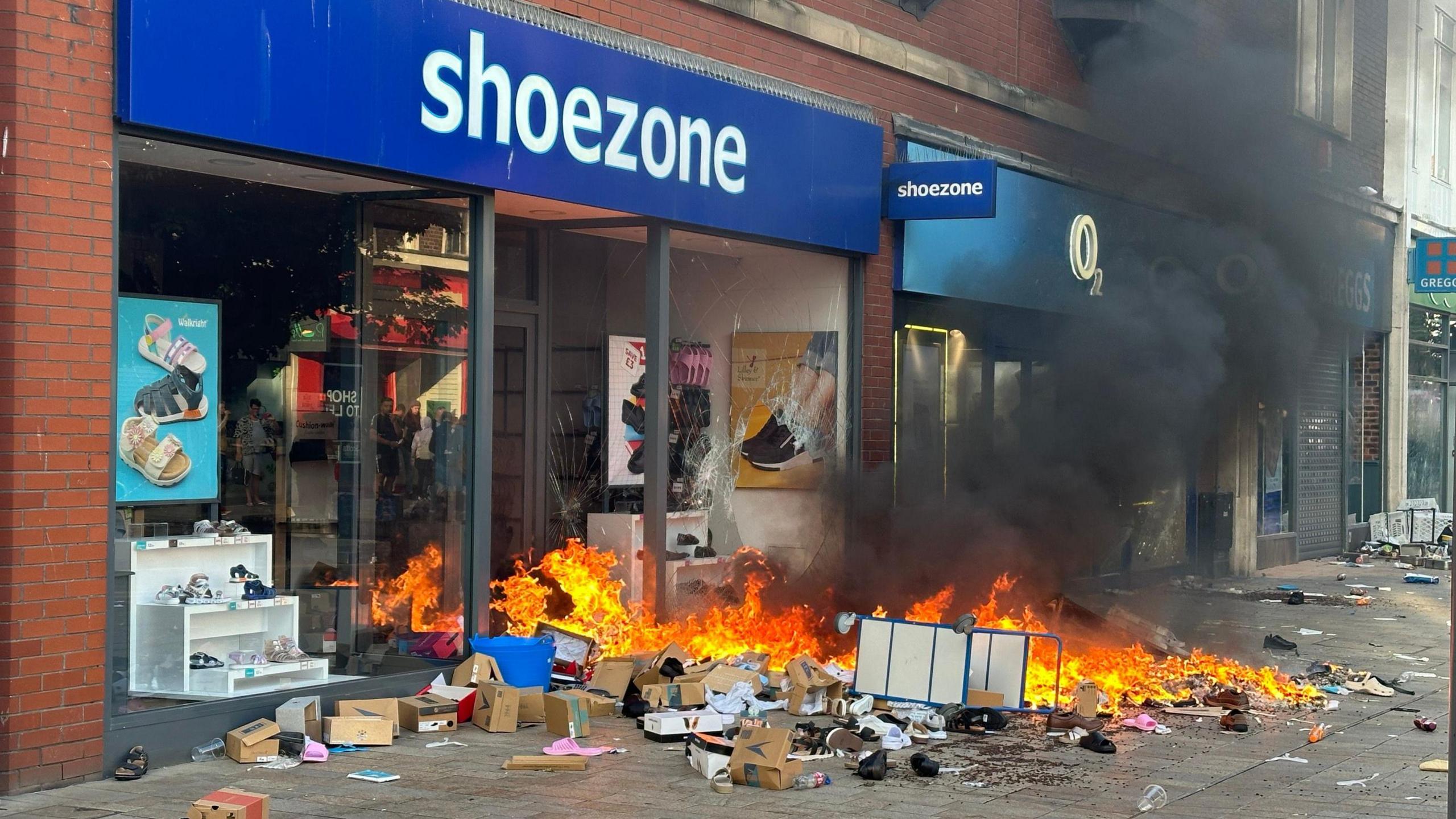 A ransacked shoe shop in Hull with a smashed front window and a pile of burning shoeboxes outsdie.