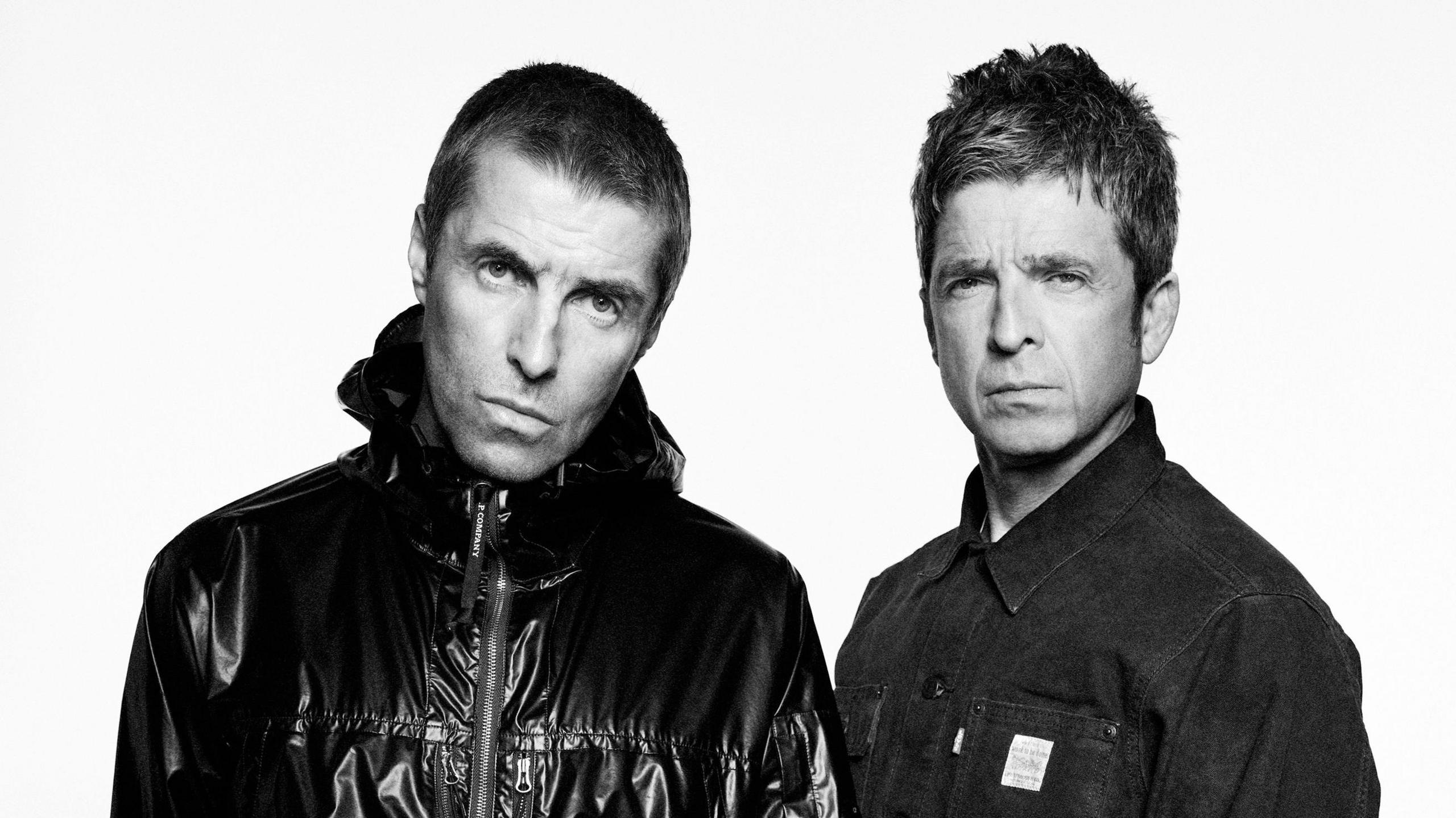 A black and white image of Liam and Noel Gallagher. Liam on the left has a leather coat and Noel is wearing a denim shirt