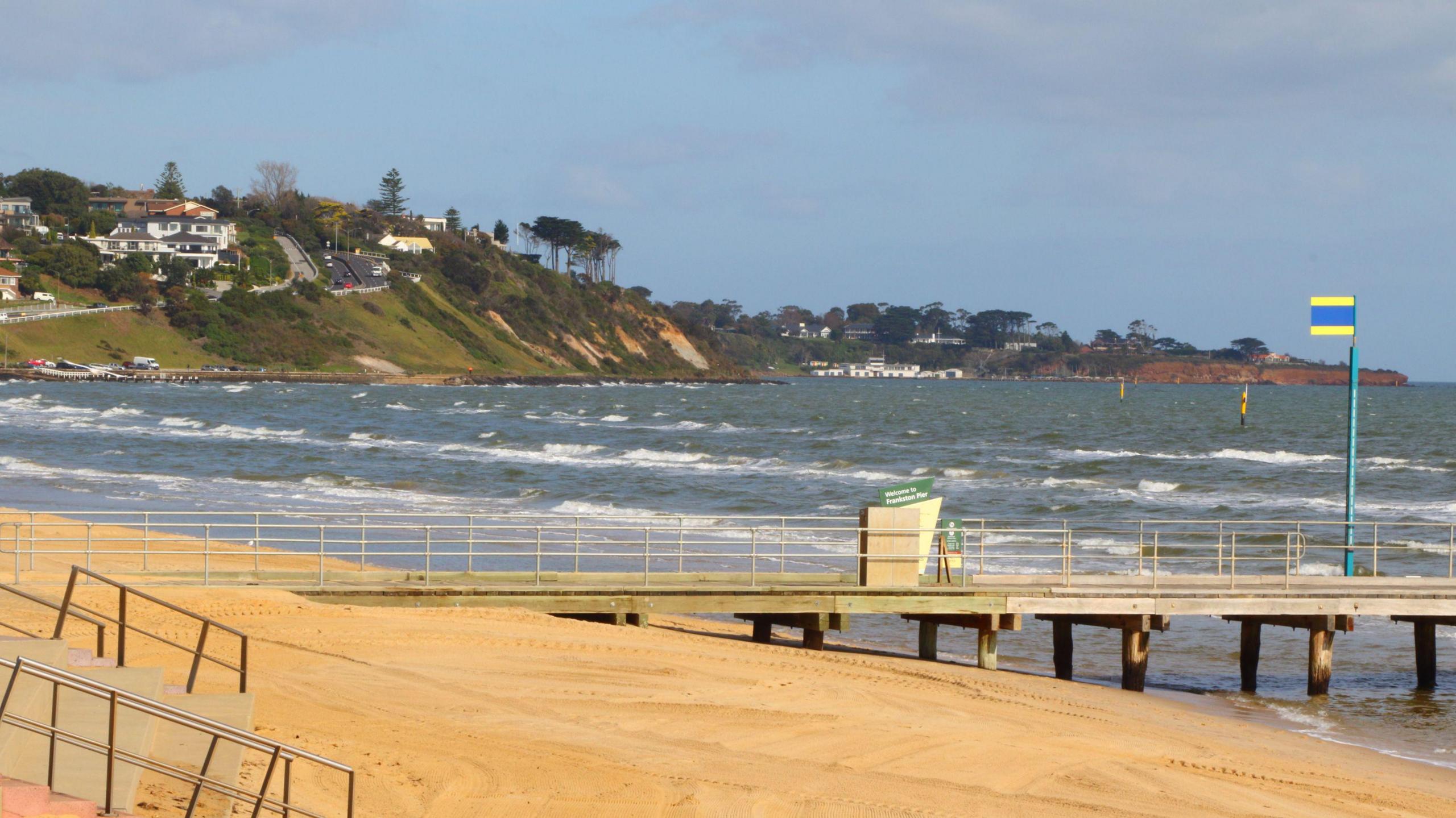 A sandy beach with a pier and waves in the background.