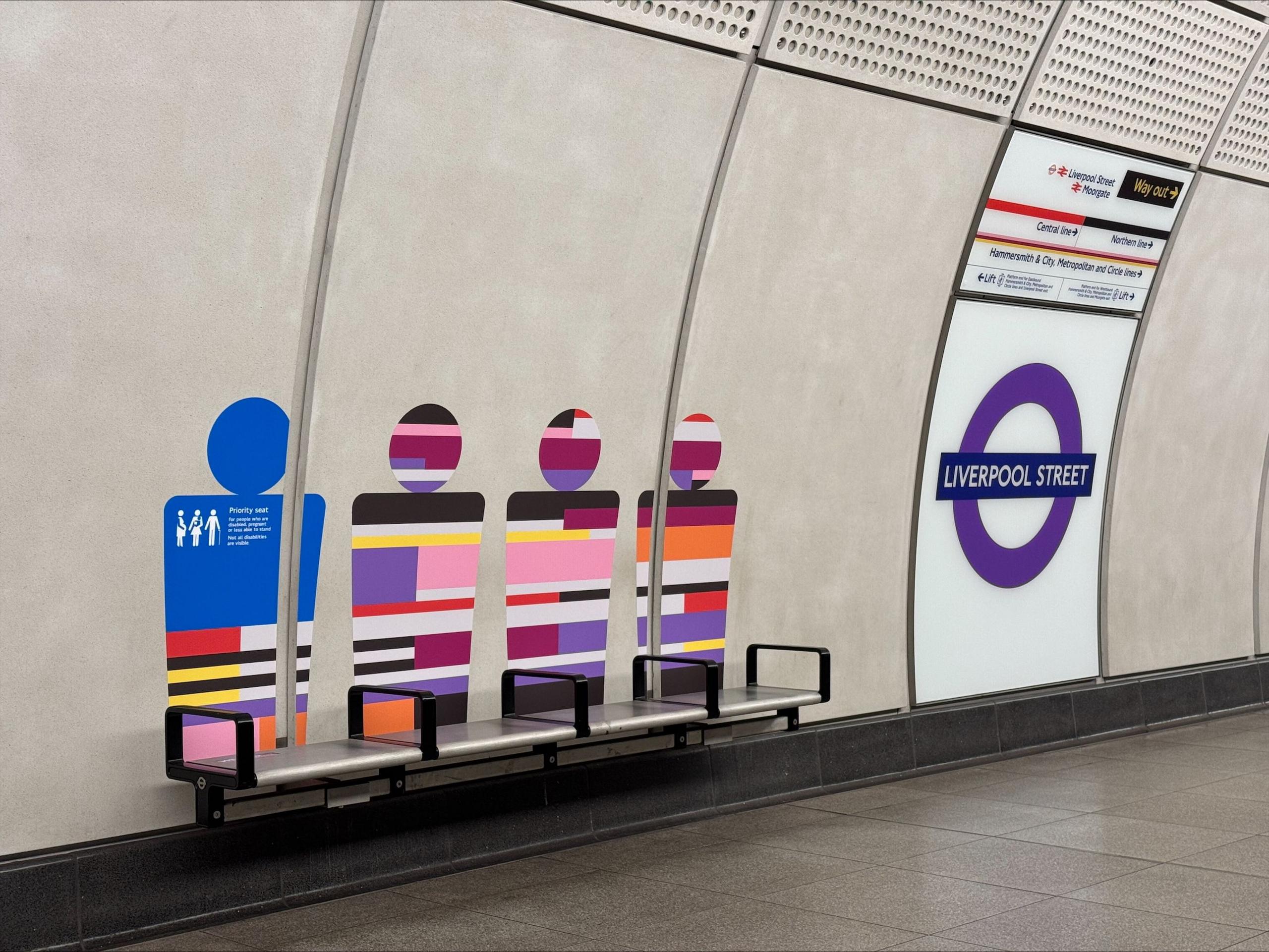 Colourful outline of people on wall of Liverpool Street Elizabeth line platform above silver seats with black armrests