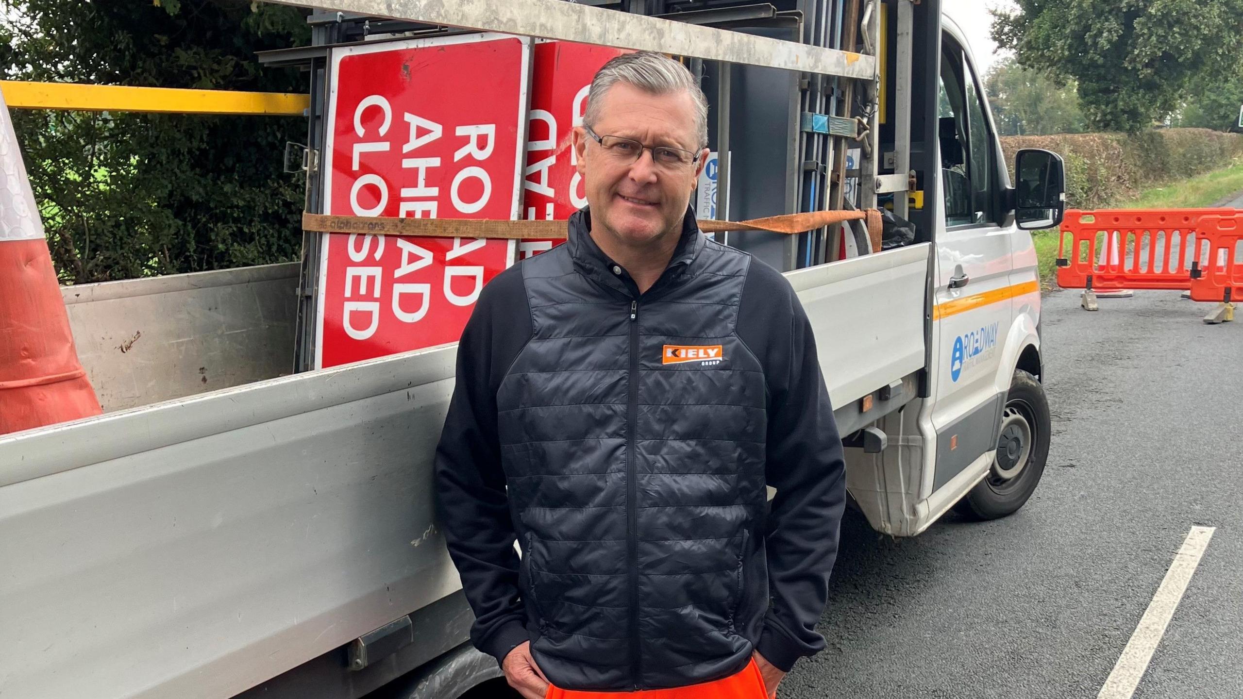 Neil Levett, from Kiely Group, stands on the road in front of a vehicle carrying road signs 