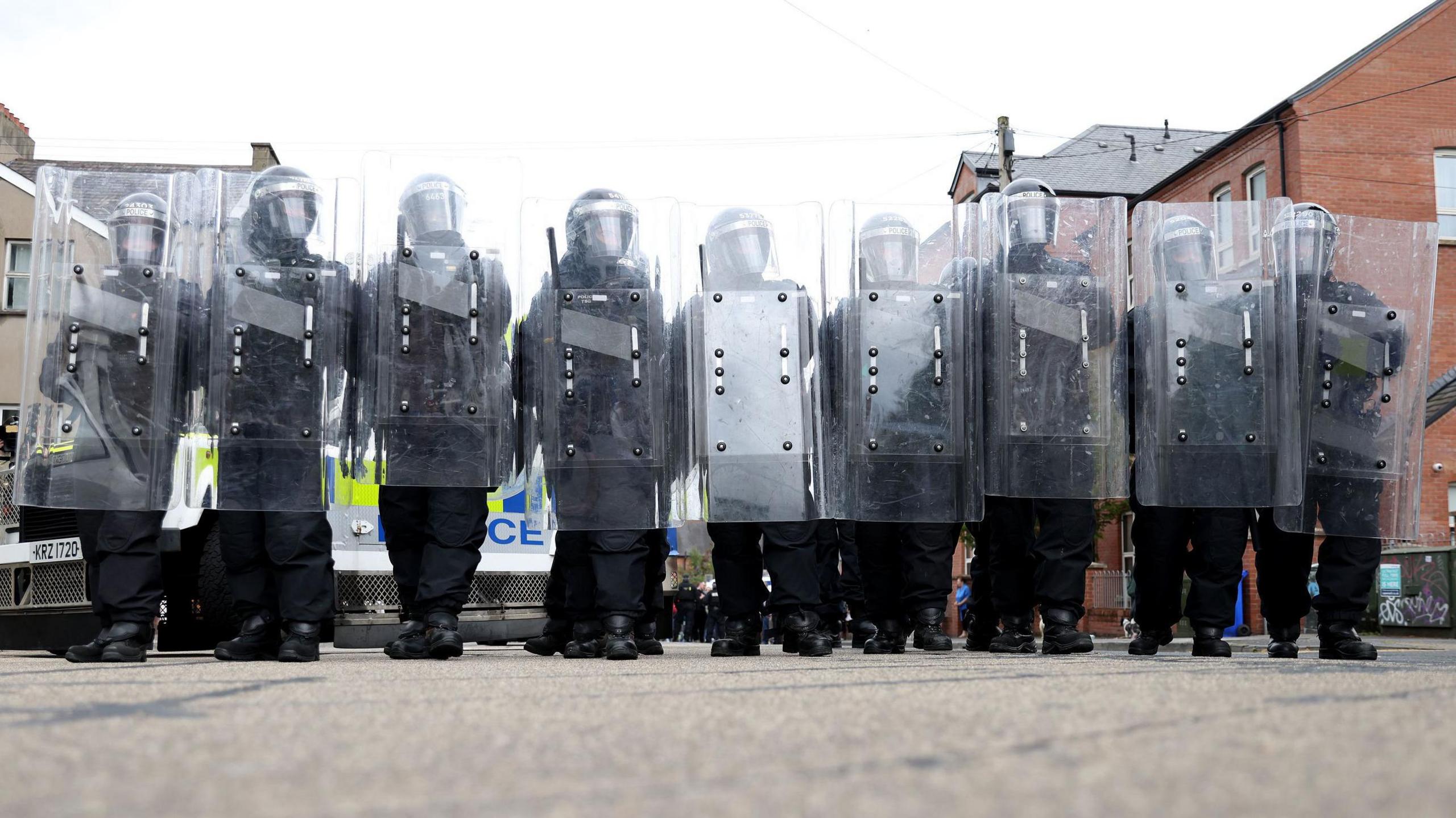 Nine riot police officers stand behind their shields, with full riot gear, in Belfast on Saturday 3 August