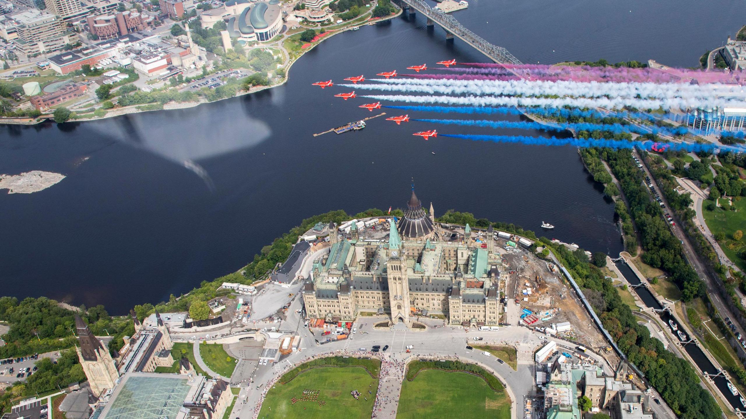 Red Arrows team flying over the green-roofed Confederation Building in Ottawa with water and bridge in background