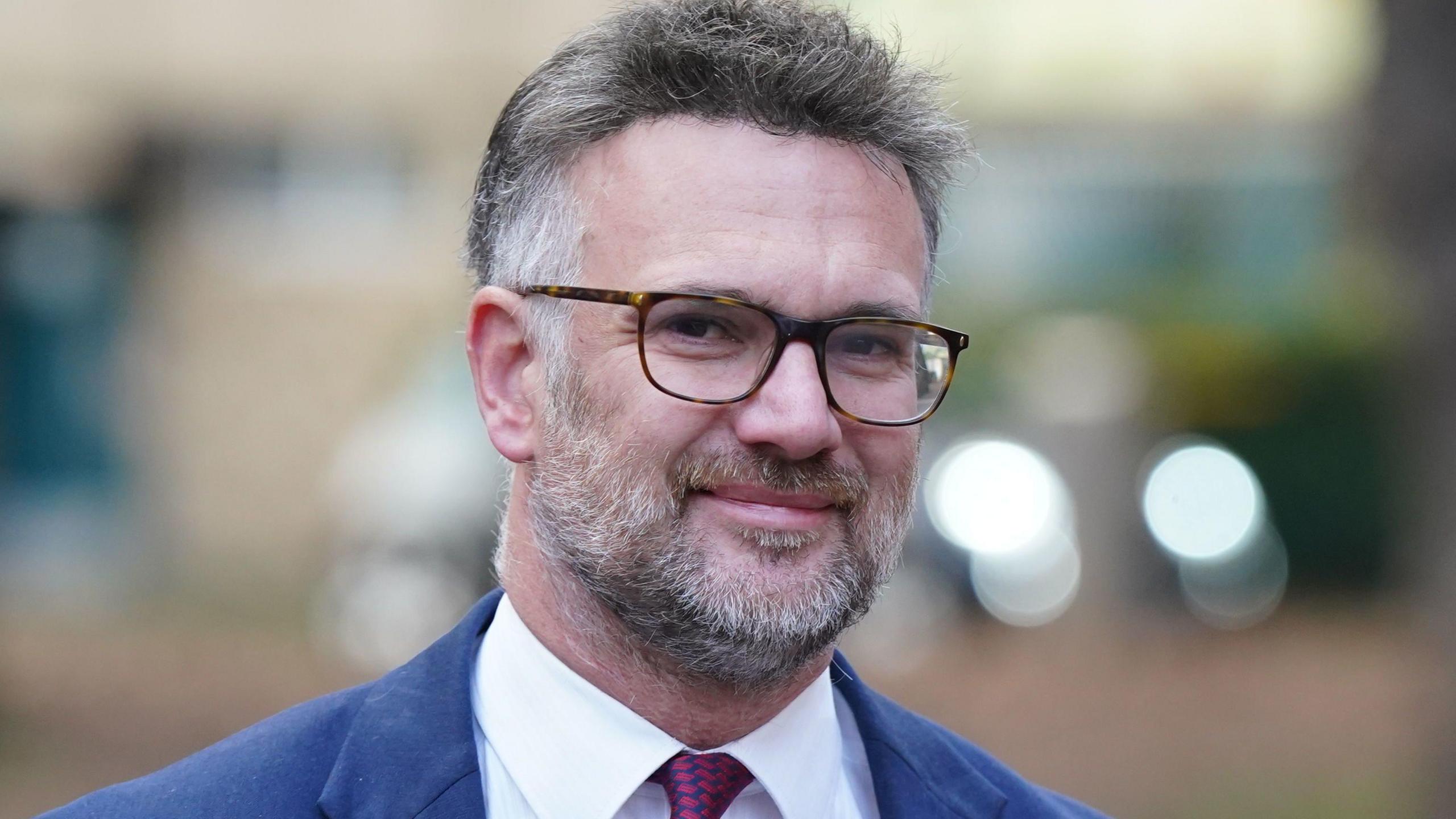 An image of Charles Hanson wearing glasses, a blue suit and red tie