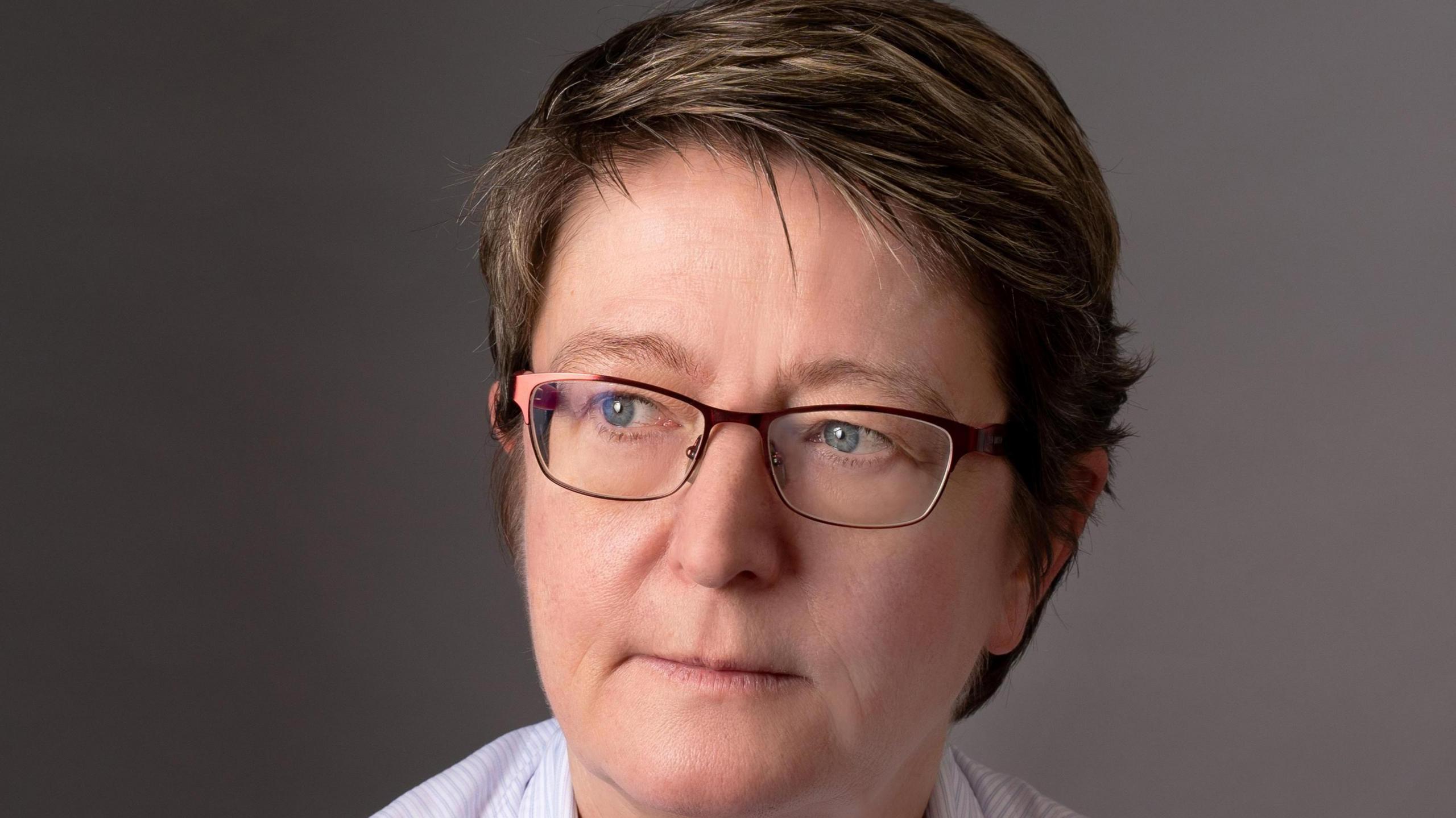 A woman with short brown hair who is wearing glasses and looking to one side of the camera.