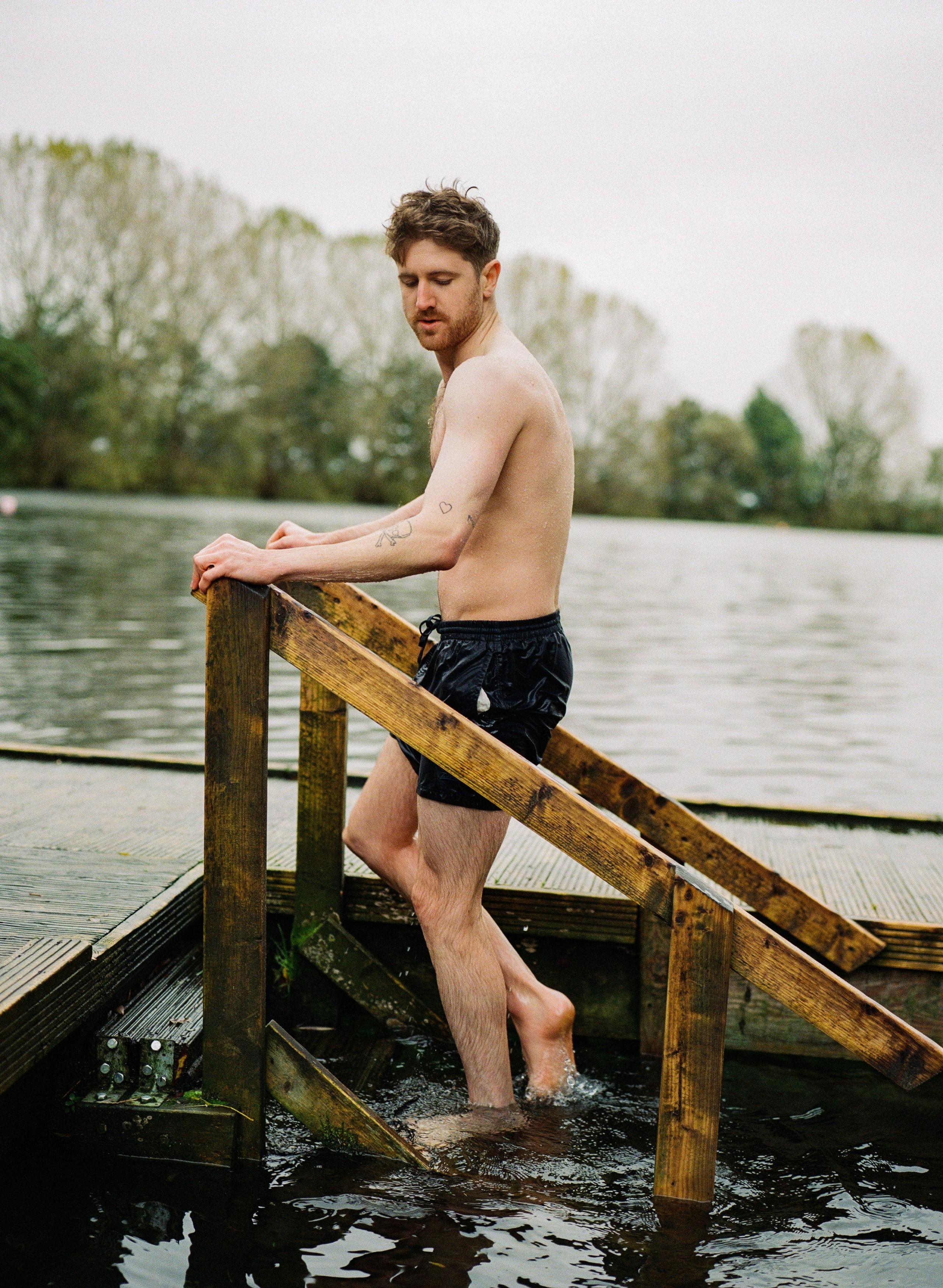 A man climbs out of open water and up onto a wooden jetty