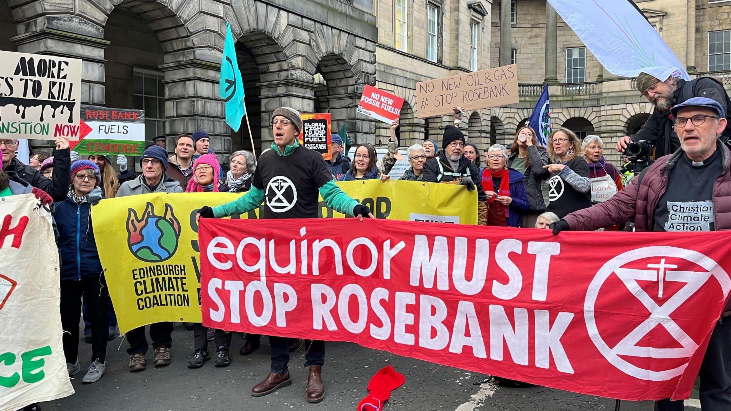 Protesters at the Court of Session in Edinburgh. They are holding a number of banners saying things like EQUINOR MUST STOP ROSEBANK and ROSEBANK FUELS GENOCIDE while shouting and chanting.