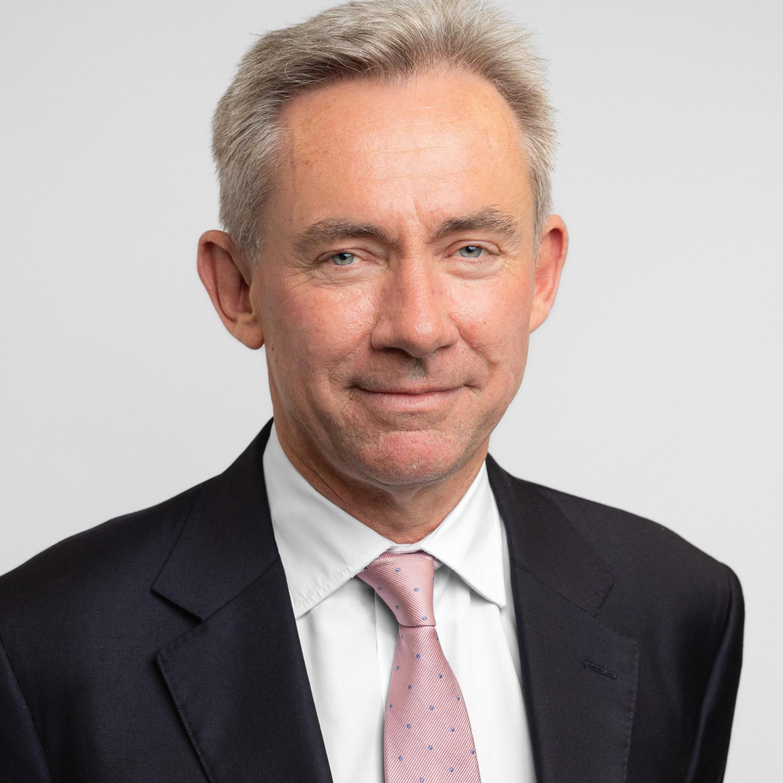 Mark Temple is wearing a dark suit and pink tie.