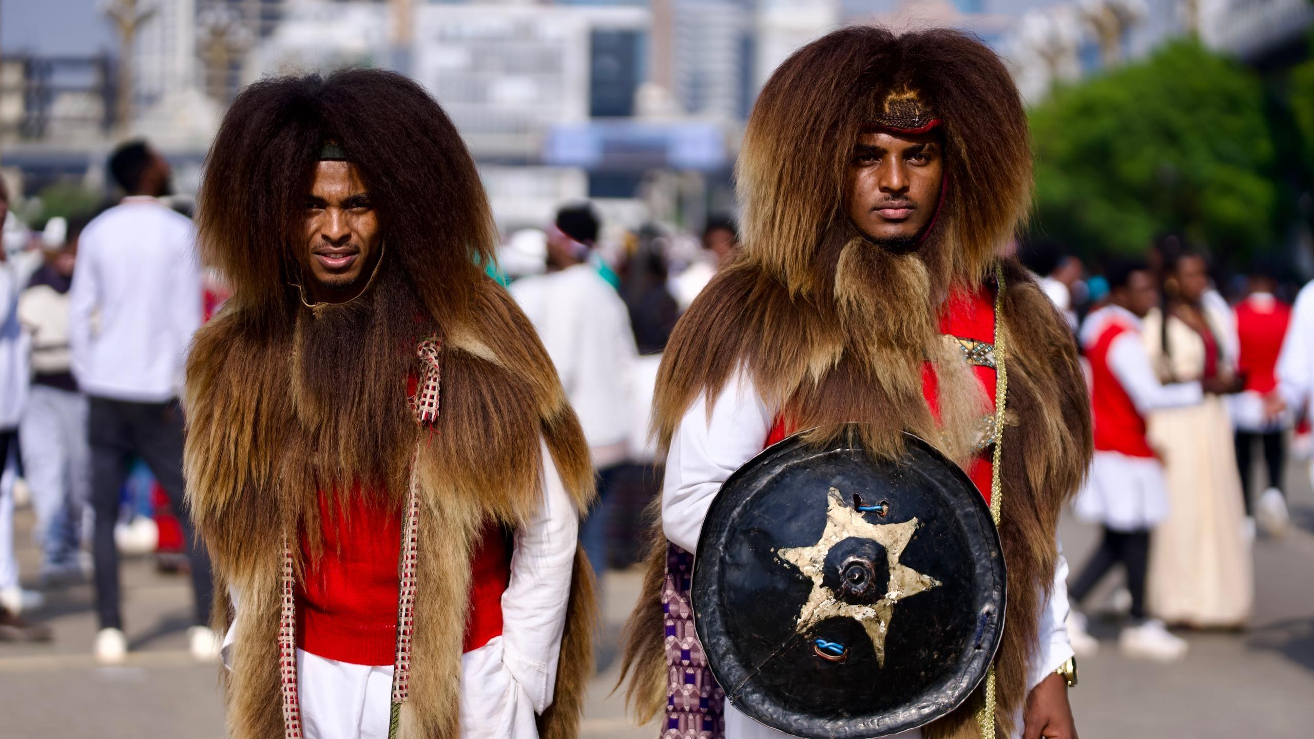 Two men wear fur on their heads and across their shoulders. One holds a shield.