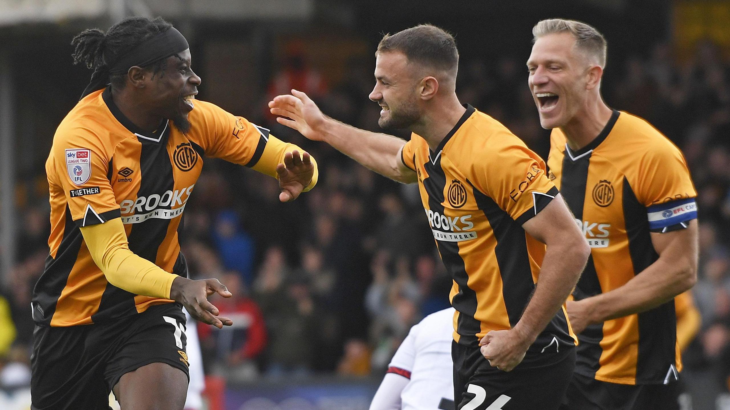 Pelly Ruddock Mpanzu of Cambridge United celebrates scoring with James Gibbons and Michael Morrison