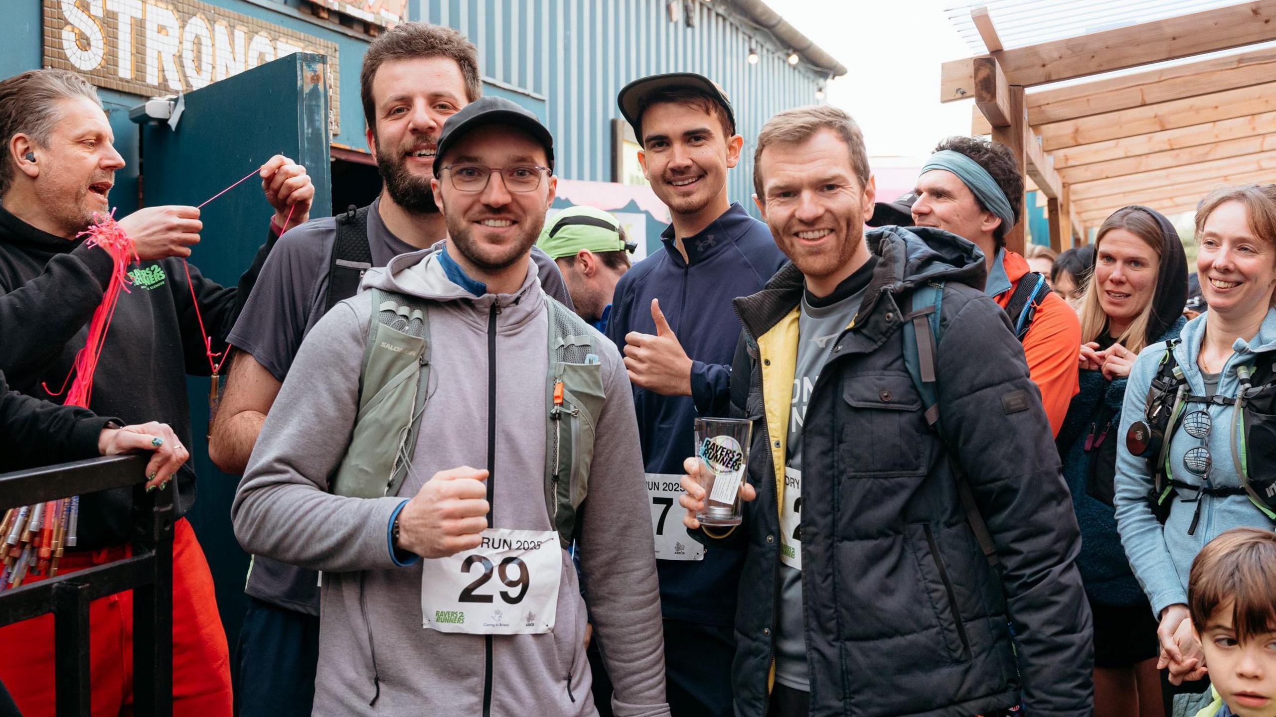 A group of people who took part in the Ravers2Runners event in Bristol smile as they group together for the camera. Some of them have race numbers pinned to their torsos, and the group is made up of a variety of ages and contains both men and women