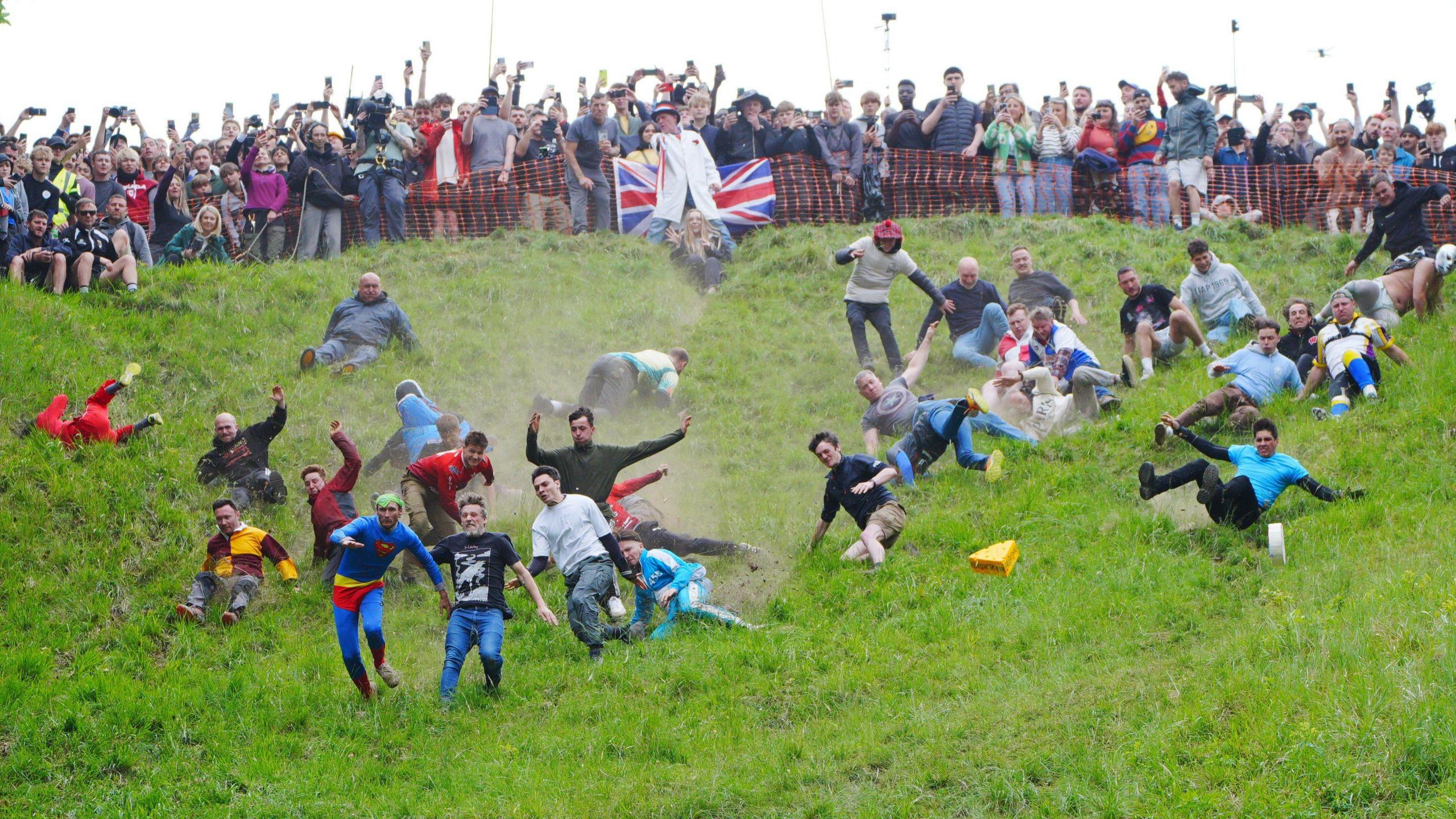Contestants tumble down Cooper's Hill in Gloucestershire during the annual cheese rolling race. It is the men's race, and is being watched by a large crowd at the top of the hil