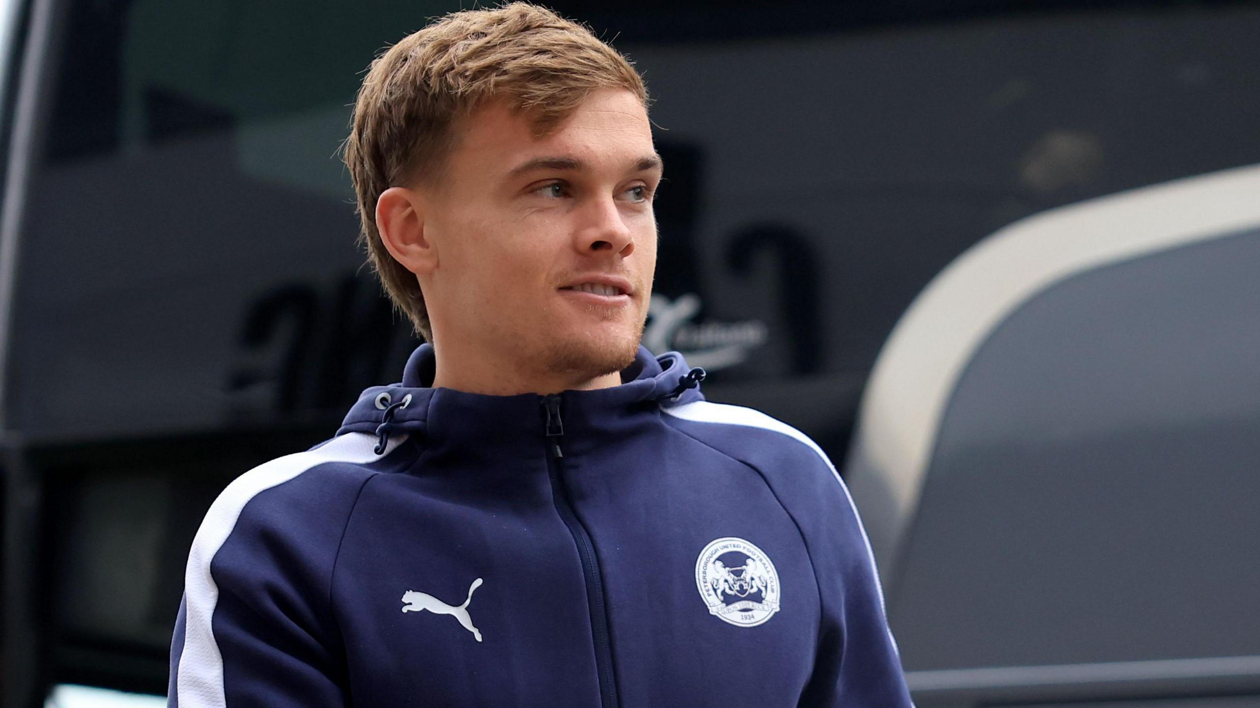 Archie Collins, wearing a tracksuit, steps off the Peterborough team bus
