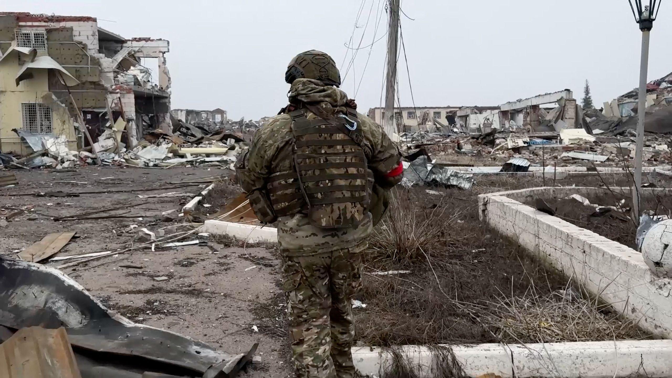 A Russian soldier, identified with red tape on his arm, walks through destroyed buildings in Loknya