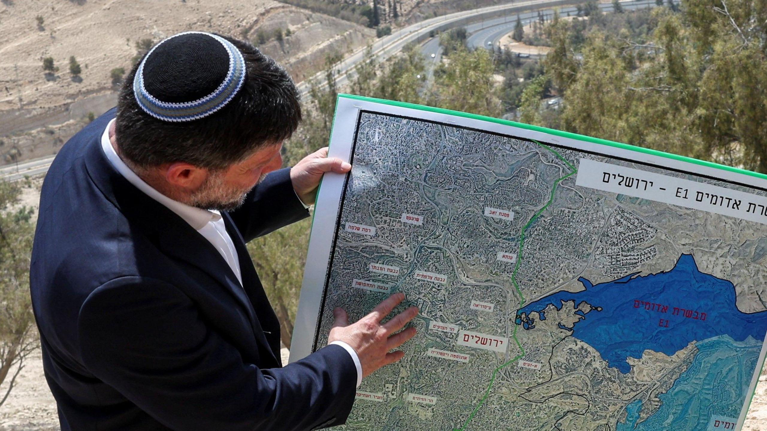 Israeli Finance Minister Bezalel Smotrich and a woman hold a map that shows the long-frozen E1 settlement scheme, that would split East Jerusalem from the occupied West Bank, on the day of a press conference near the Israeli settlement of Maale Adumim, in the Israeli-occupied West Bank, August 14, 2025.
