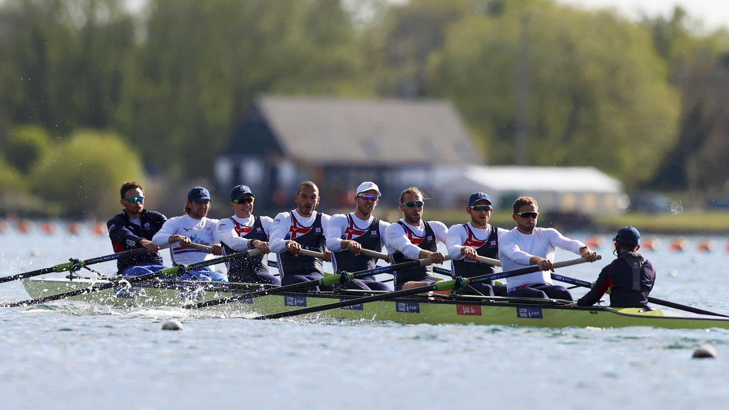 A team of eight rowers plus a coxswain on a long, green rowing boat.