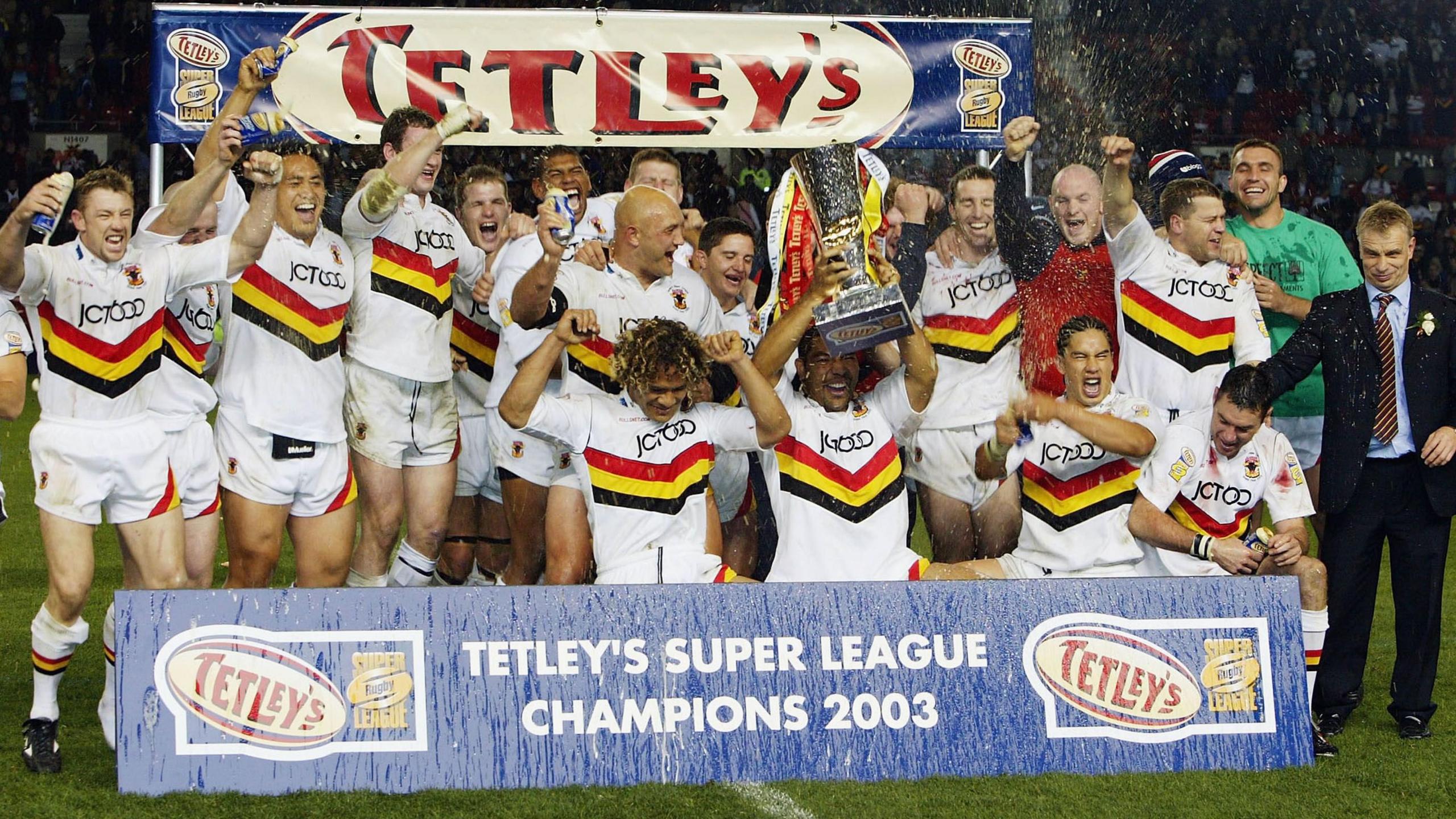 Bradford players and staff celebrate with alcohol and the Super League trophy behind the winners board after the 2003 Grand Final