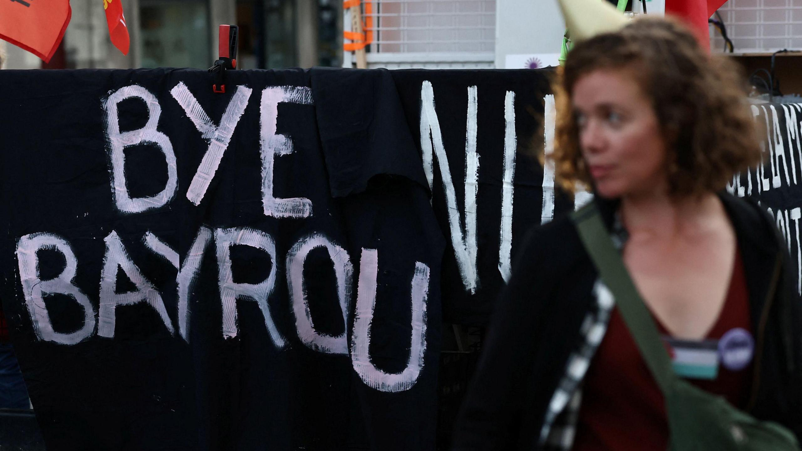The slogan "bye bayrou" is painted on a black sheet outside France's national assembly as a woman looks on.
