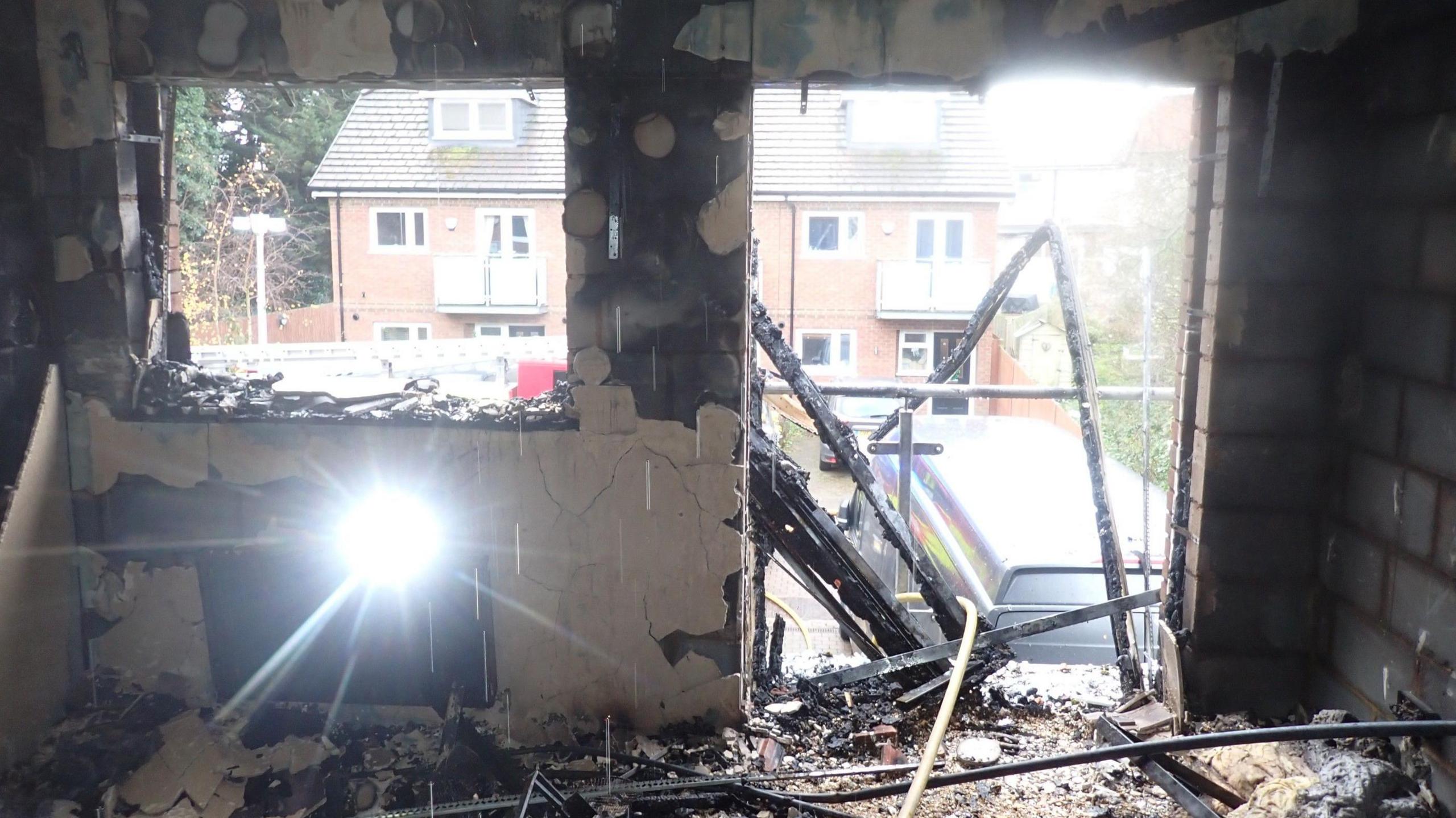 A burnt room with debris all over the floor, windows broken and exposed brick. 