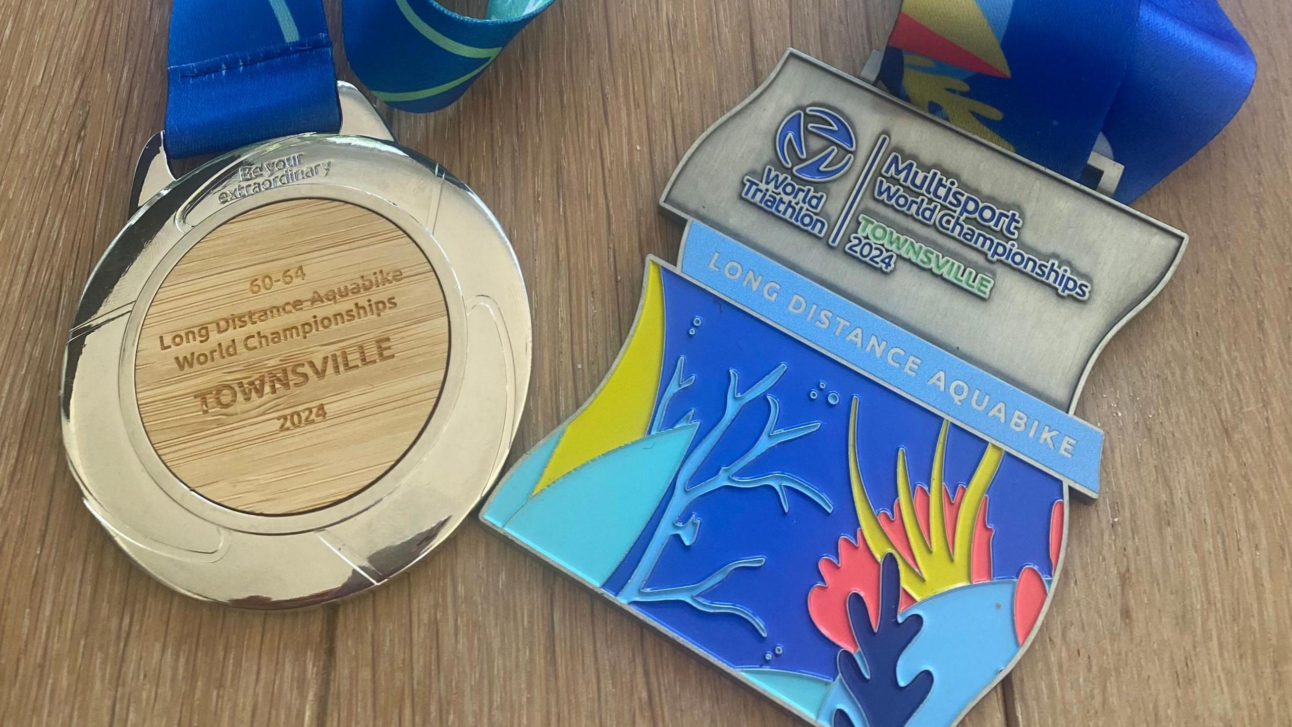 A gold medal with 'long distance aquabike world championships Townsville 2024' engraved on it. Another medal to the right, with a world triathlon emblem for people who took part in the race.  