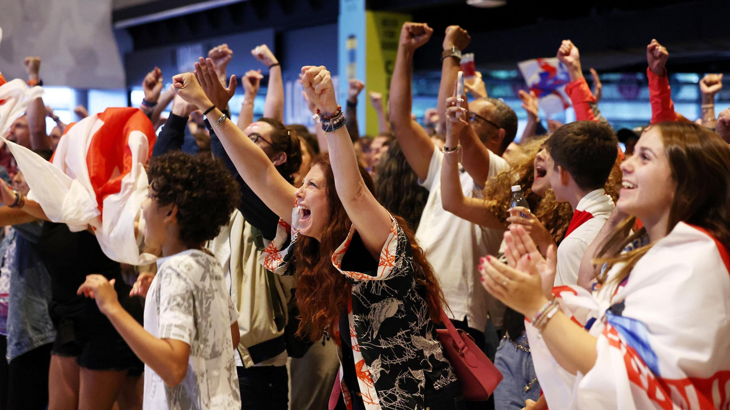 A group of football fans, mostly young women, cheer with their arms aloft as they watch England play Spain in the final of the European Championships in the sports bar at Ashton Gate Stadium in Bristol