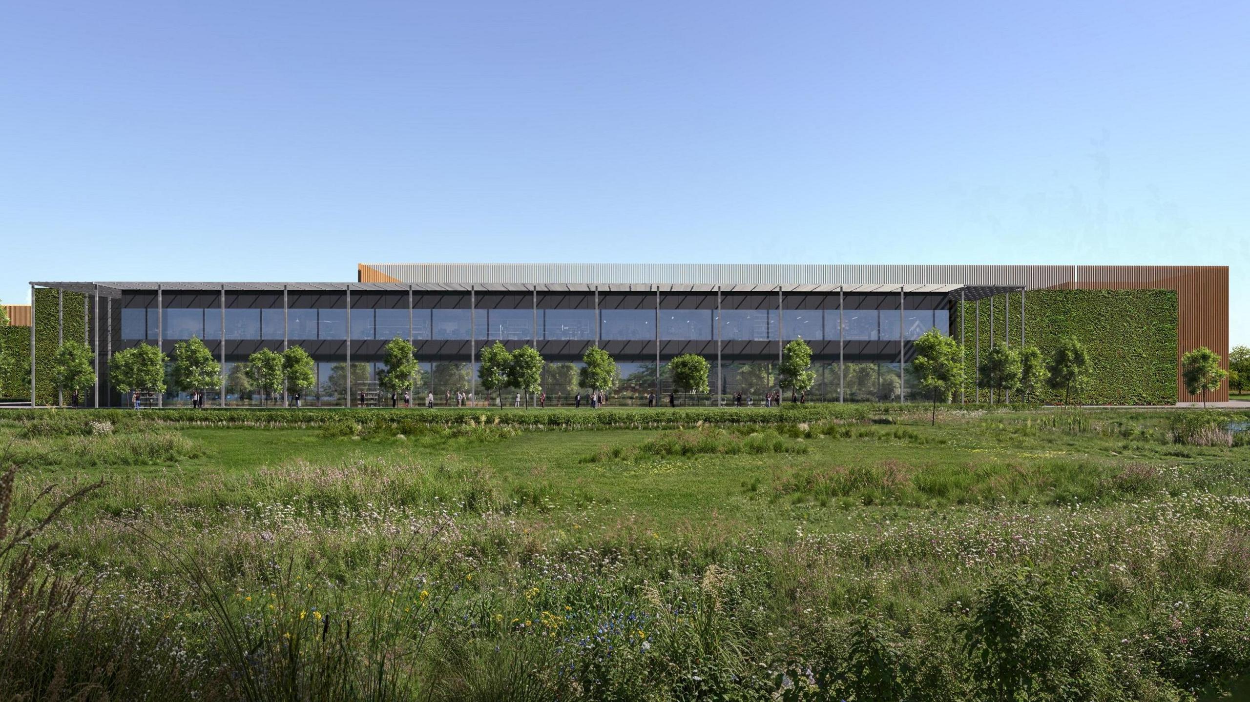 A wider shot of a data centre building showing most of its length. It is sitting on a green field and parts of the building are covered in green foliage. It is surrounded by trees