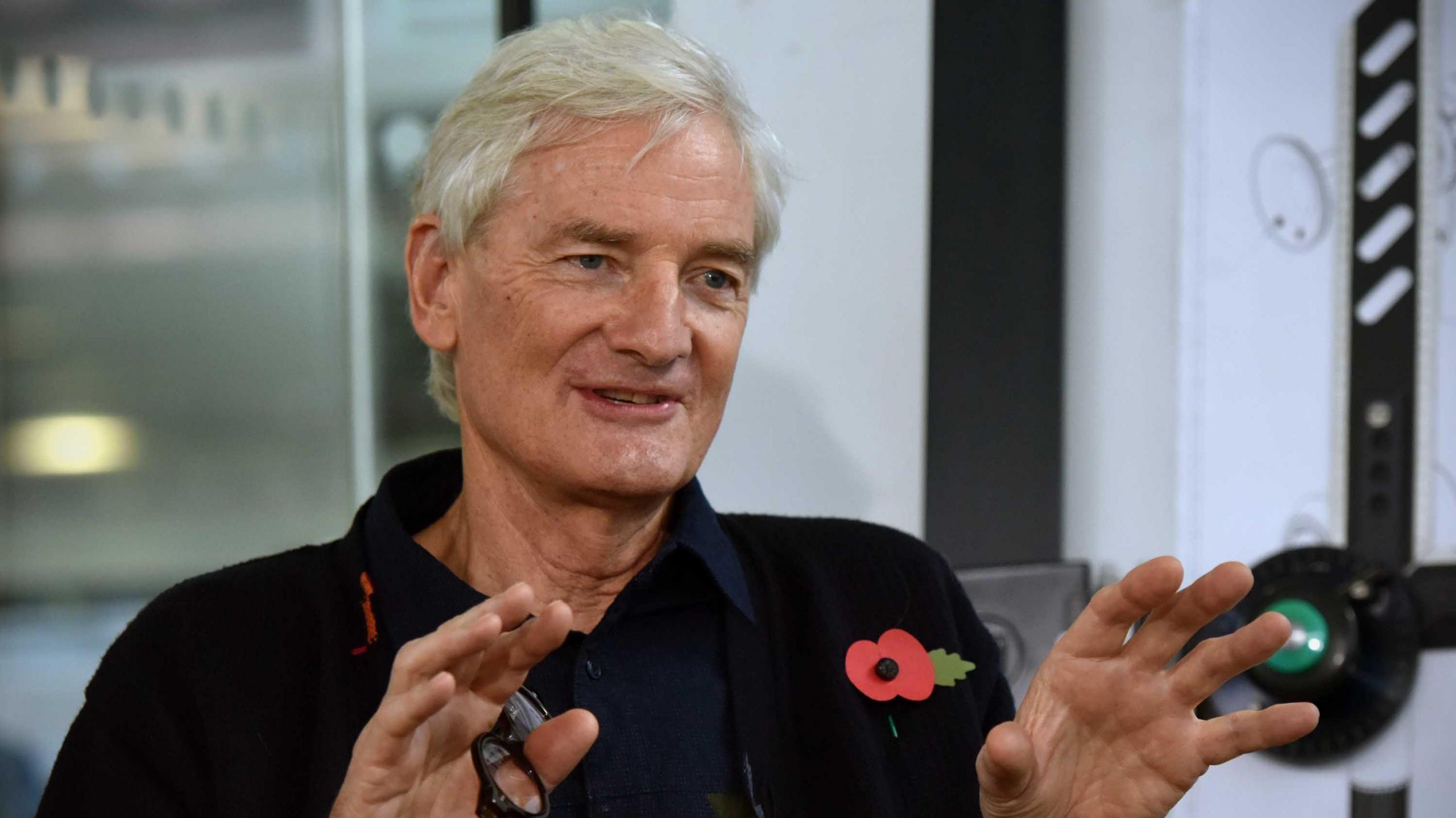 Sir James Dyson smiling whilst gesturing. He is wearing a poppy on his black jacket.