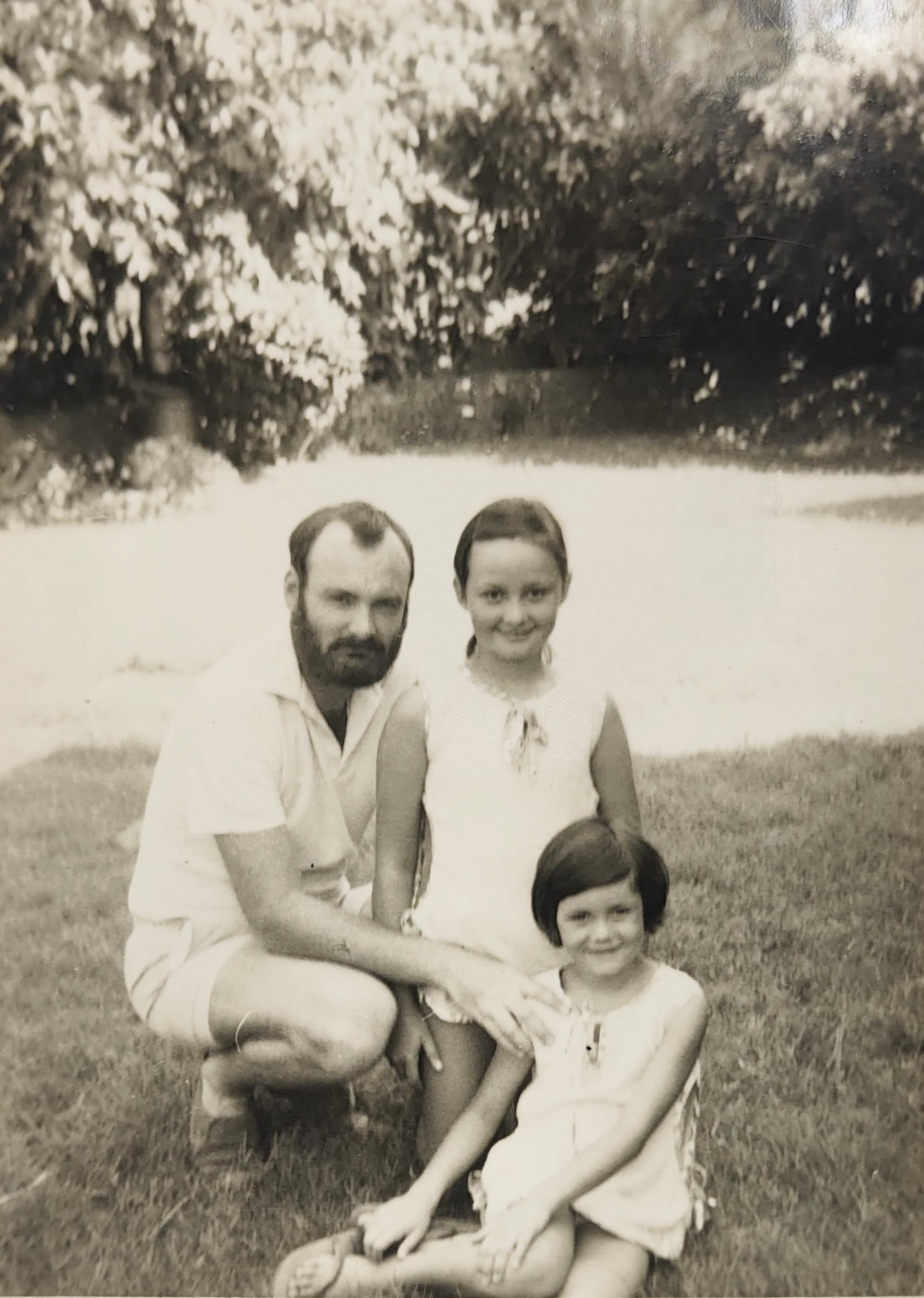 Ten year-old Michele in the centre of a black and white picture from 1972 with her father to the left and her younger sister in front. They appear to be in a sunny garden and wearing white or bright short sleeves.