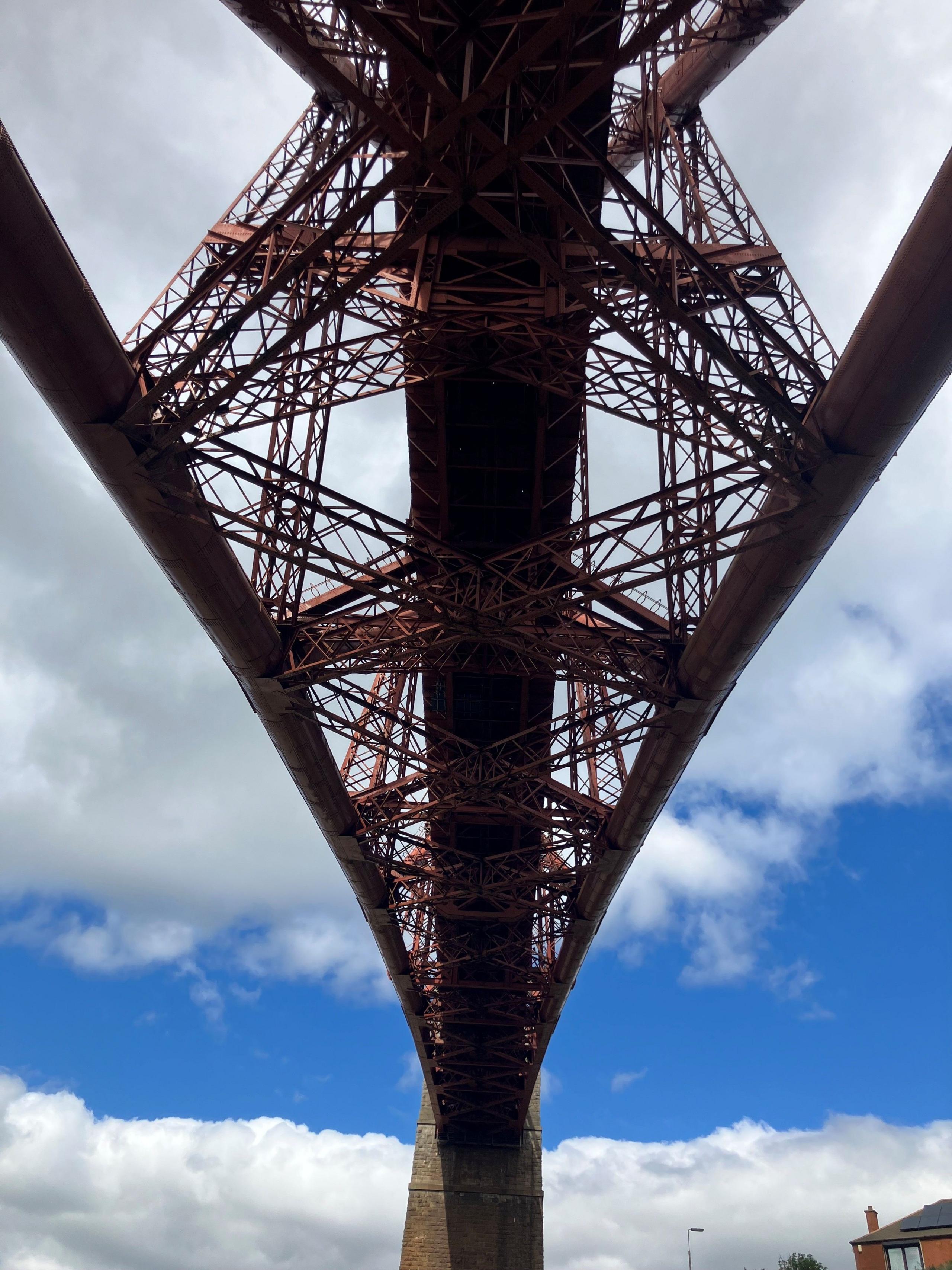Underside of the Forth Bridge with a bright blue cloudy sky behind it