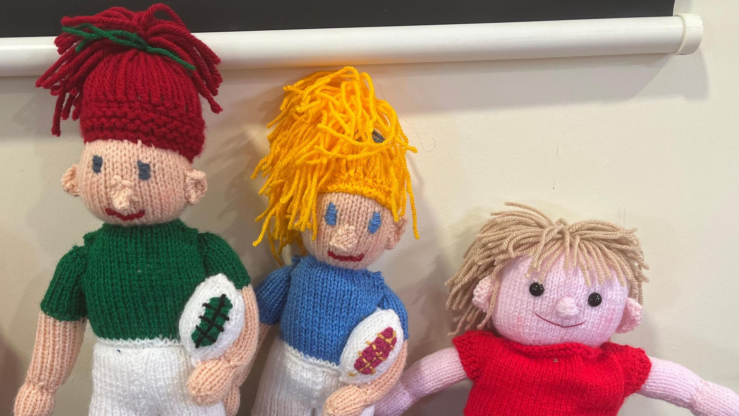 Three knitted rugby players, in a green top, a blue top and a red top.