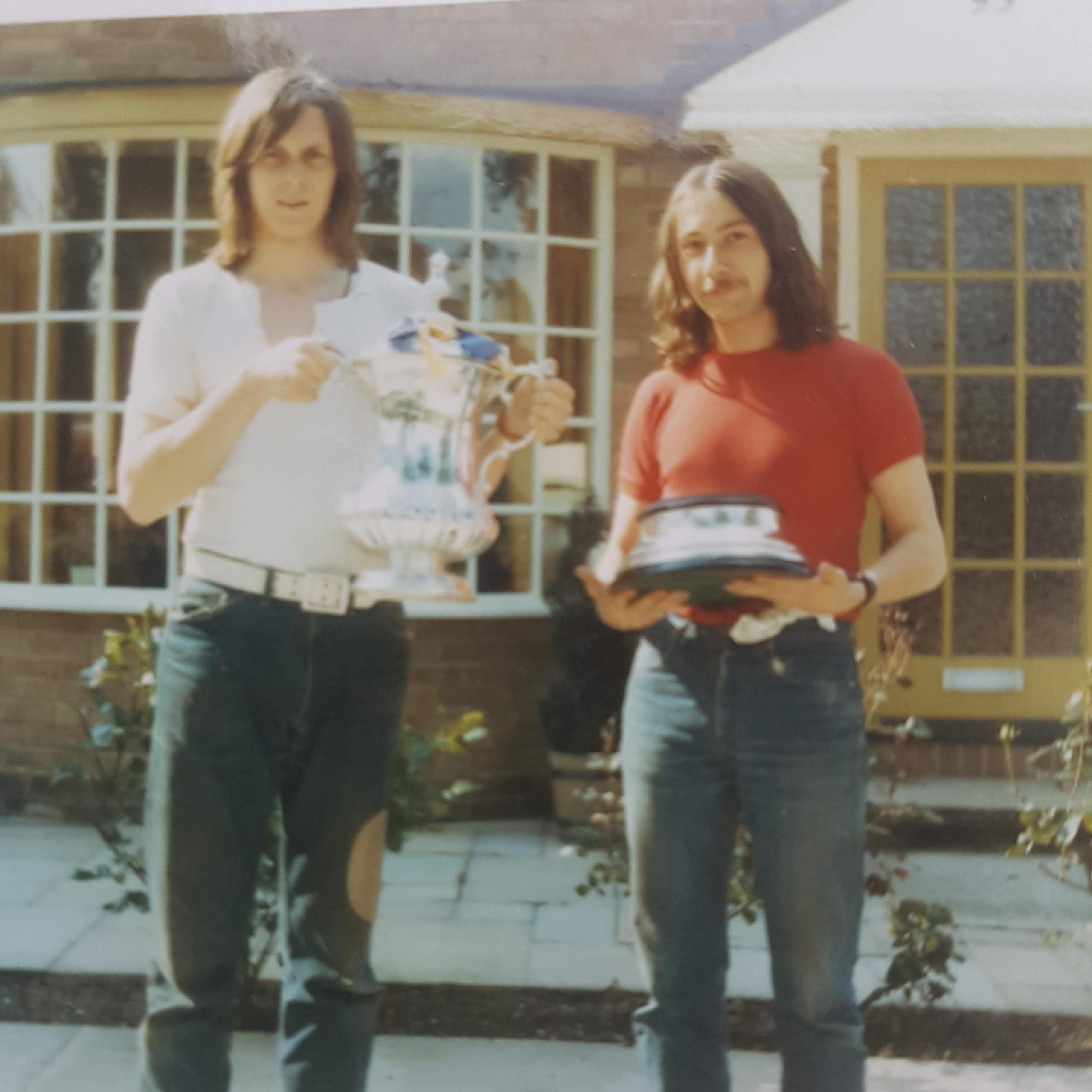 An image of two young men standing with the FA Cup, one is holding the trophy and the other is holding the base