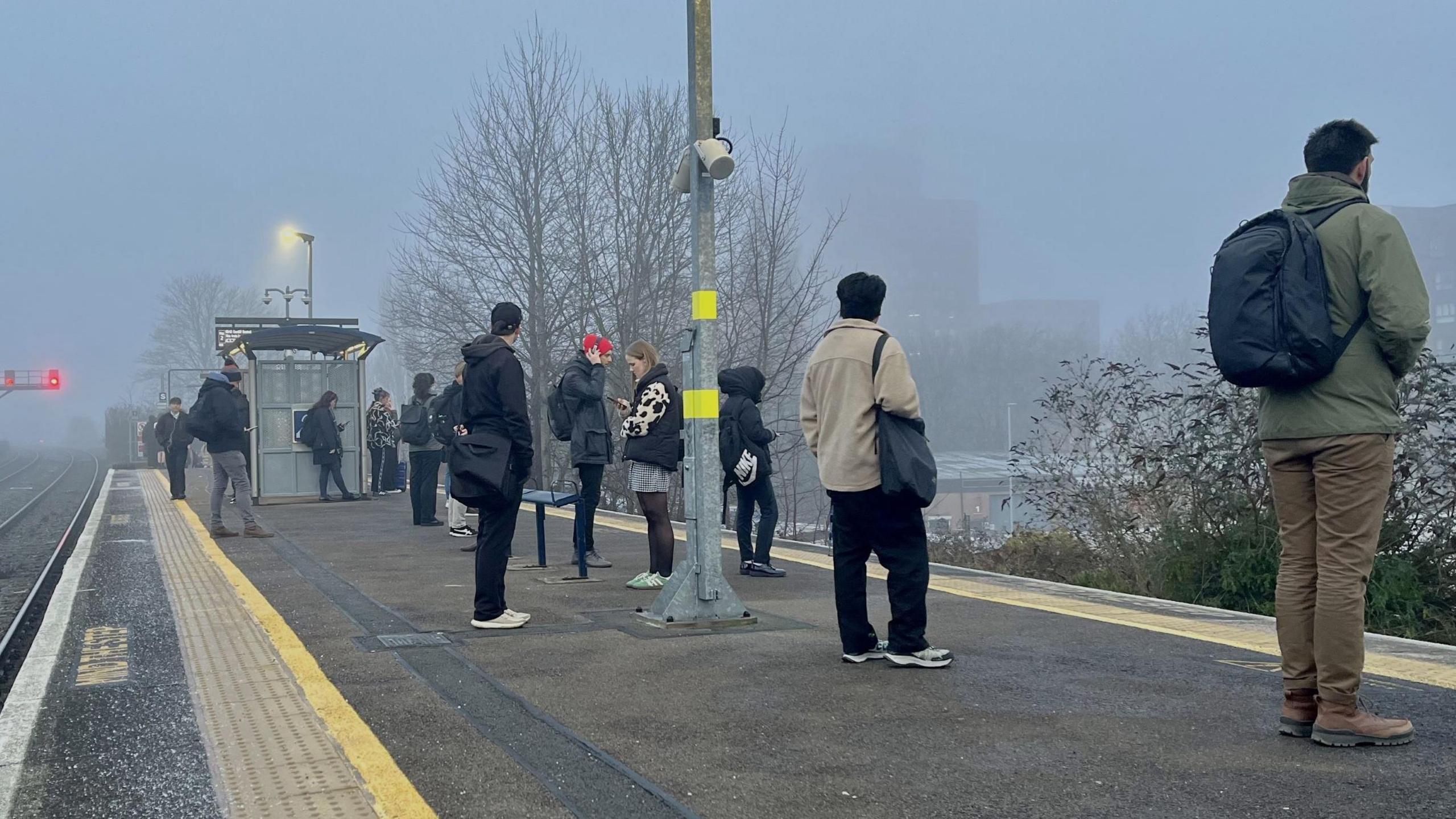 Passengers wait for a train on the platform at a misty Bedminster Station in Bristol. They are all wrapped up on a cold day